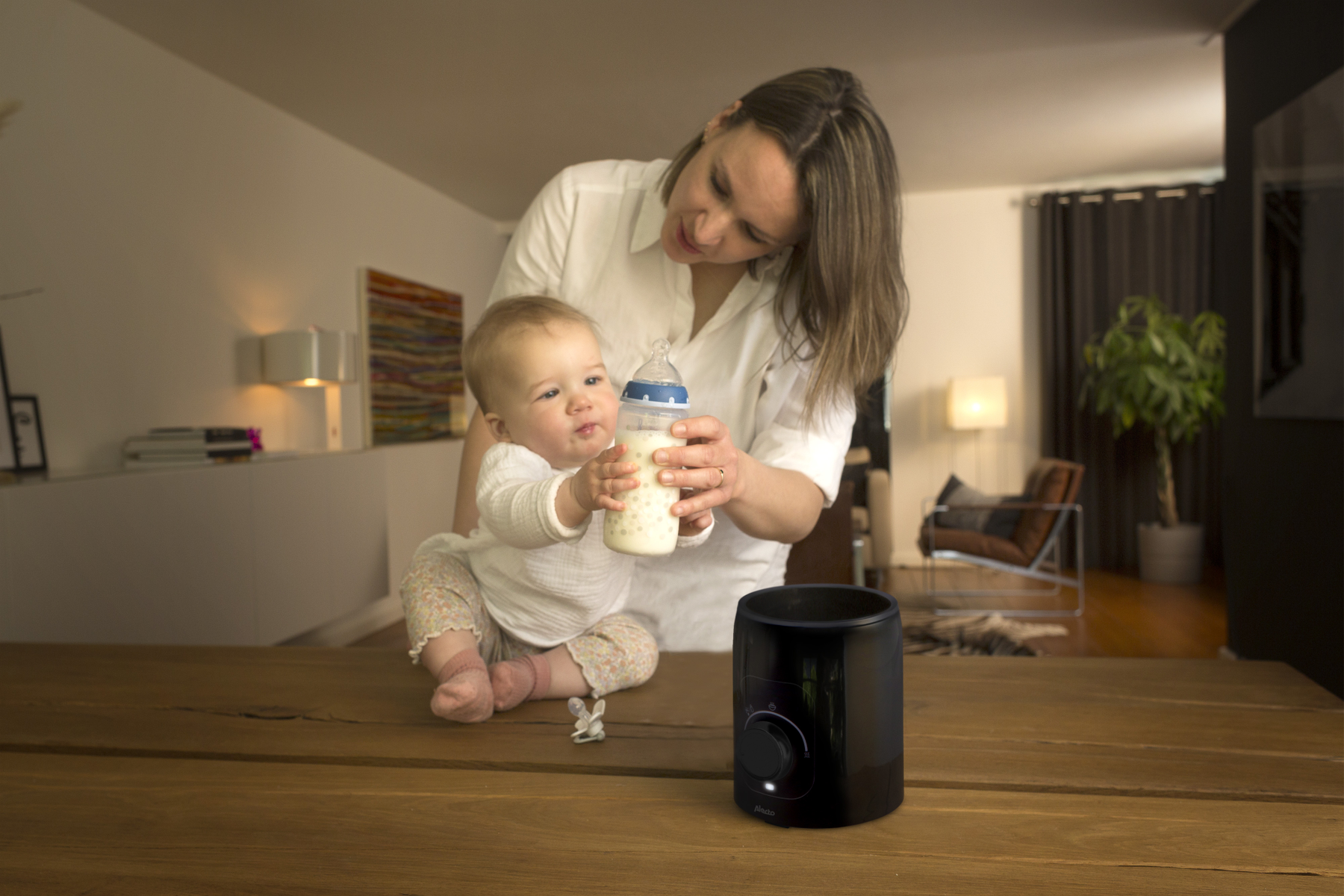 Eine Frau, die eine Babyflasche hält und ein Baby füttert, auf einem Holztisch mit einem Flaschenwärmer.