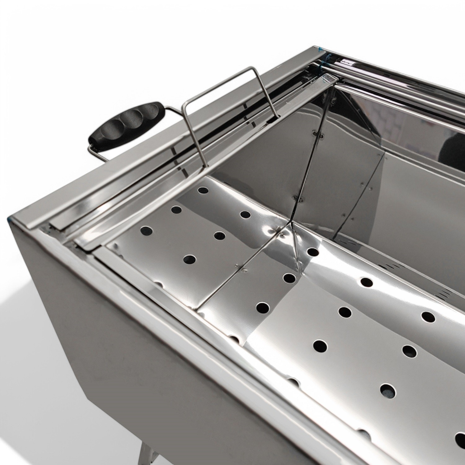 Ein Edelstahl-Grill, Innenraum sichtbar. Perforierte Basis und abgewinkelte Seiten. Weißer Hintergrund.
