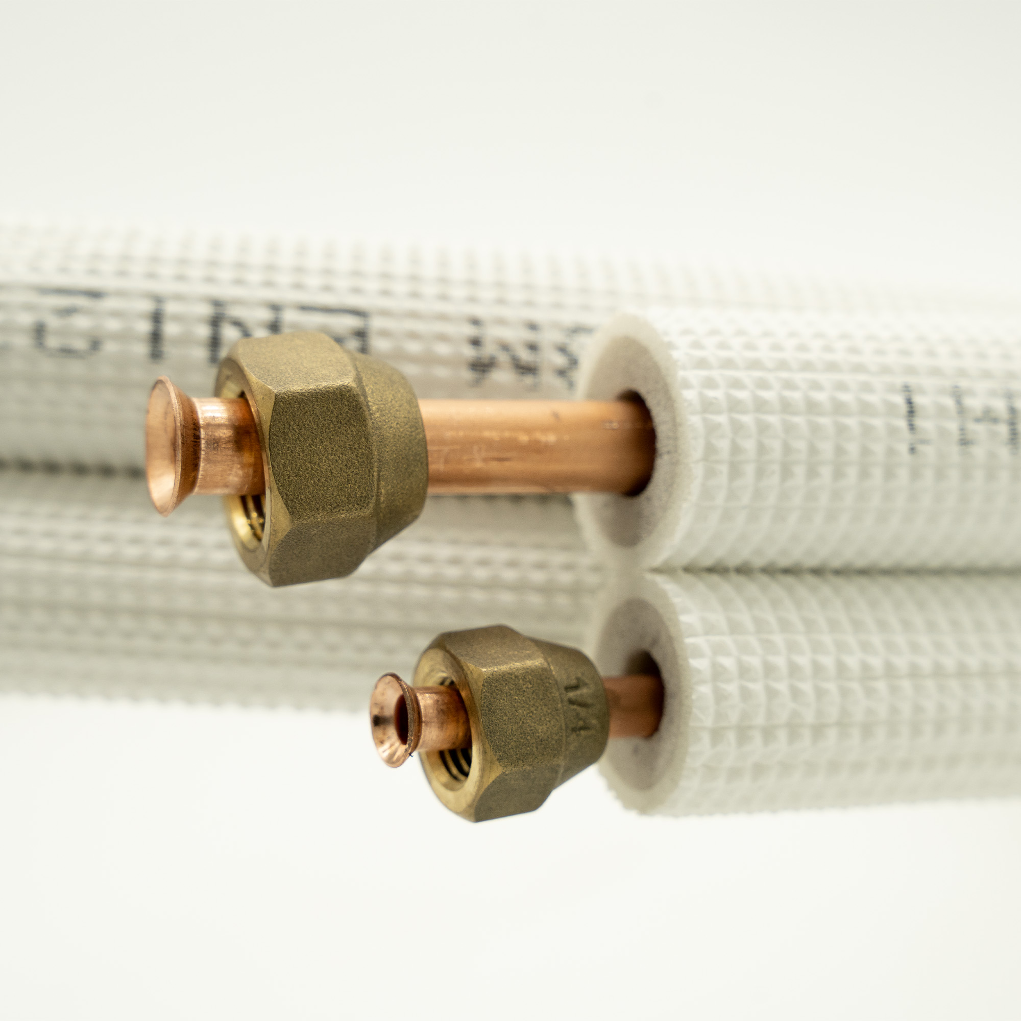 Close-up of two copper pipes with brass connectors, wrapped in white insulated material.
