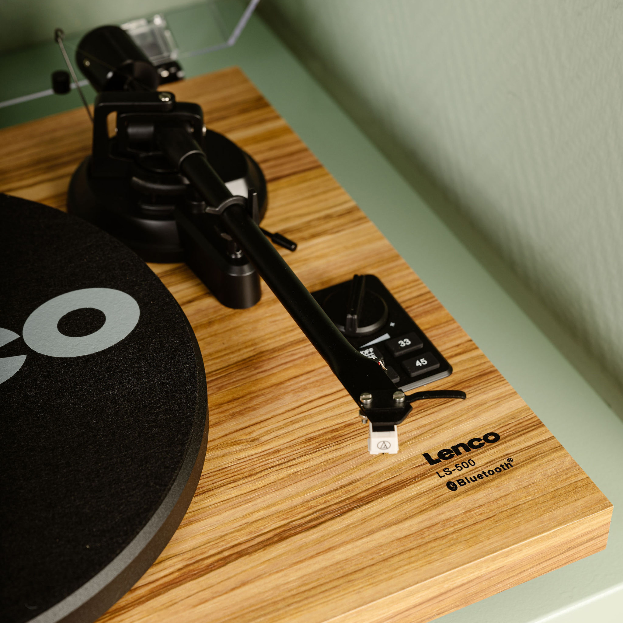 Gramofon z czarnym ramieniem i drewnianą podstawą. Widoczna nazwa marki 'Lenco'.