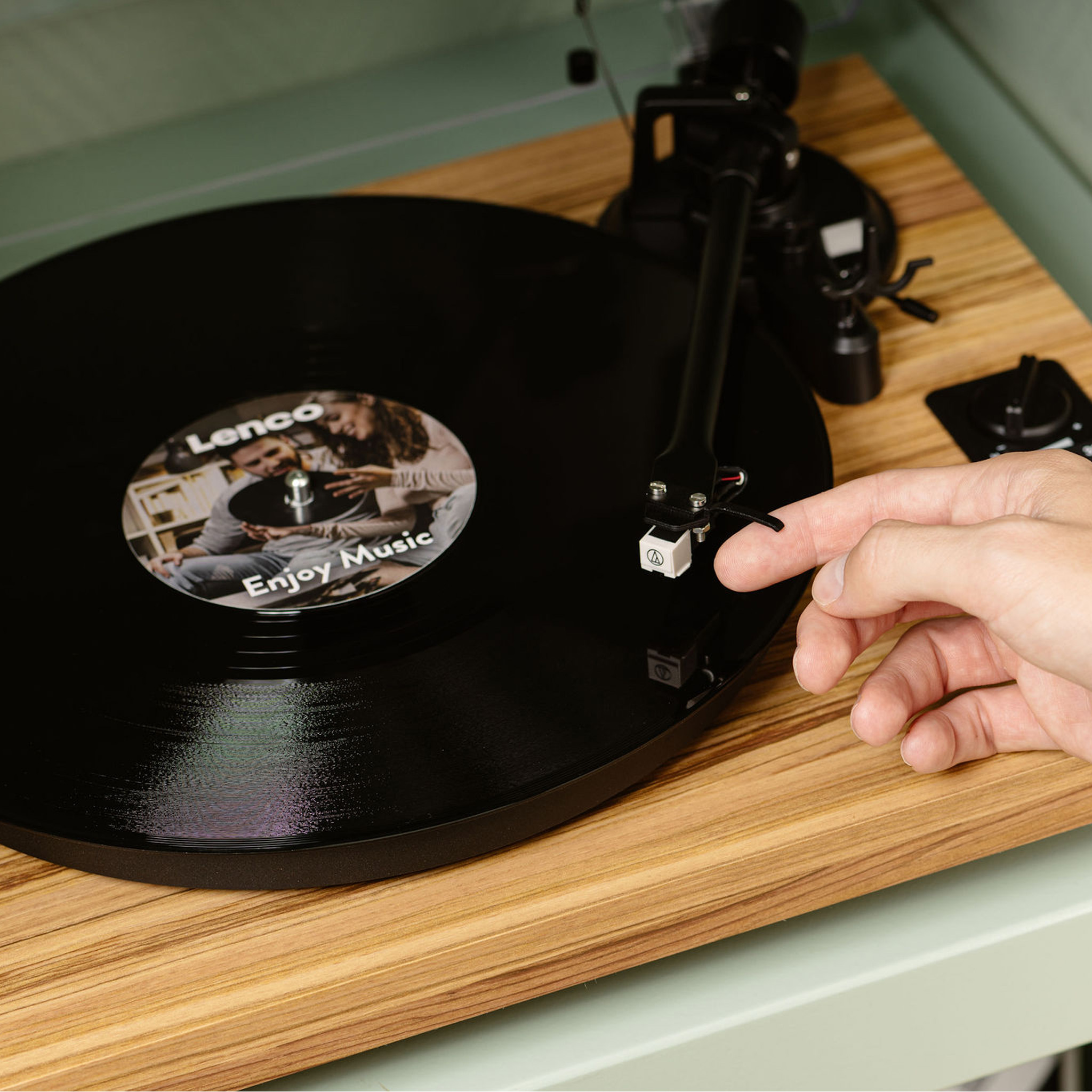 Ręka osoby reguluje igłę gramofonu na drewnianej powierzchni.