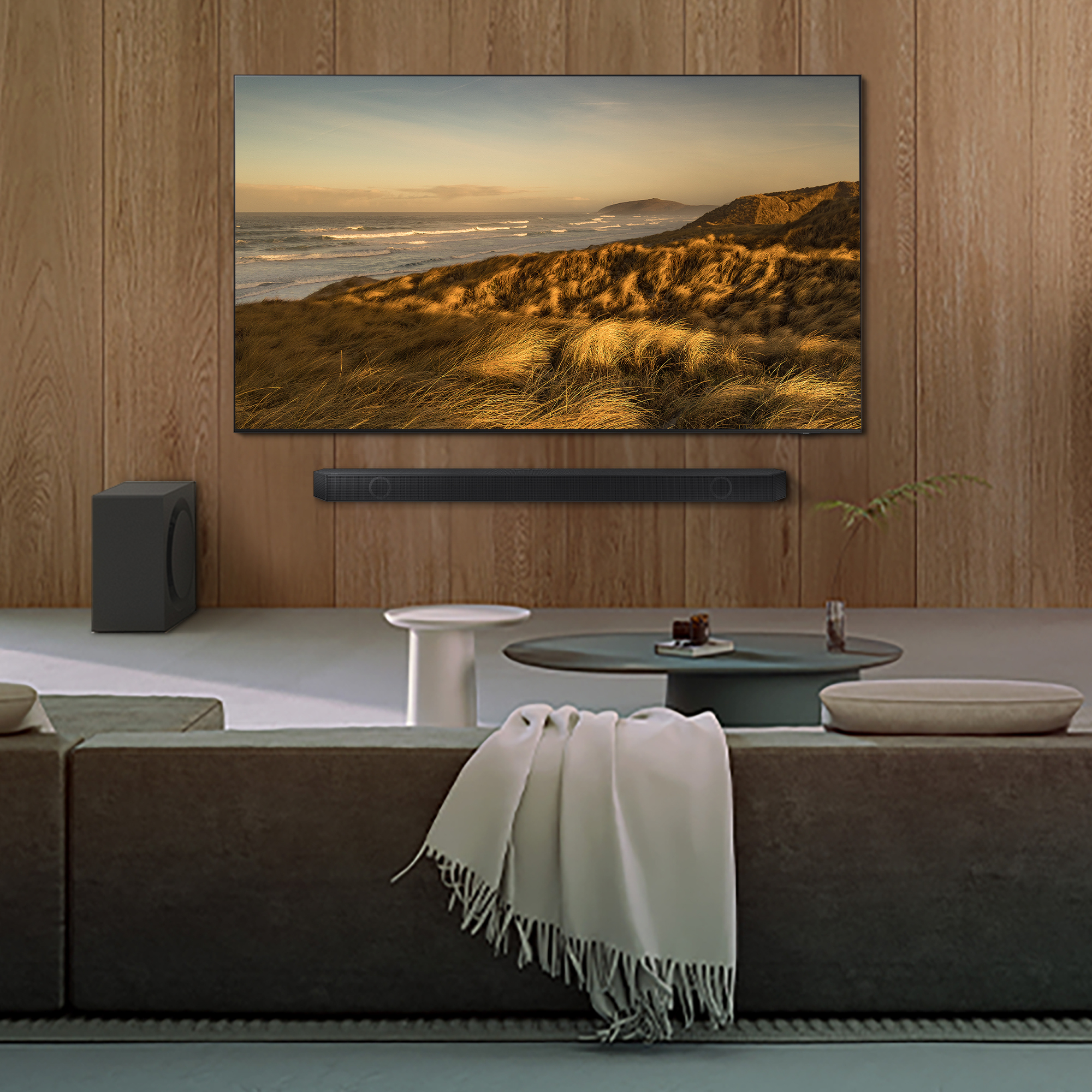 Scena di soggiorno con TV, soundbar, divano e decorazioni, con paesaggio costiero sullo schermo.