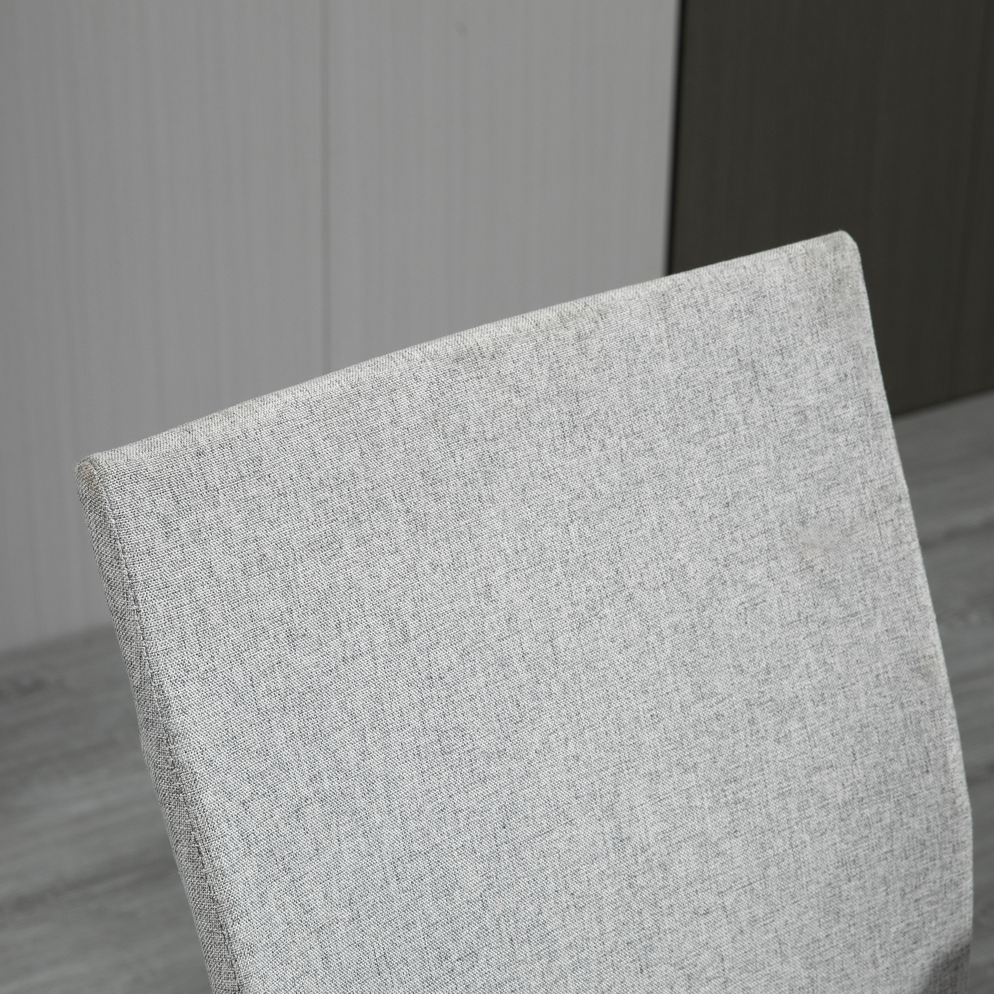 Primo piano dello schienale di una sedia. Tessuto grigio, chiaro e strutturato. Leggermente angolato, con sfondo bianco.