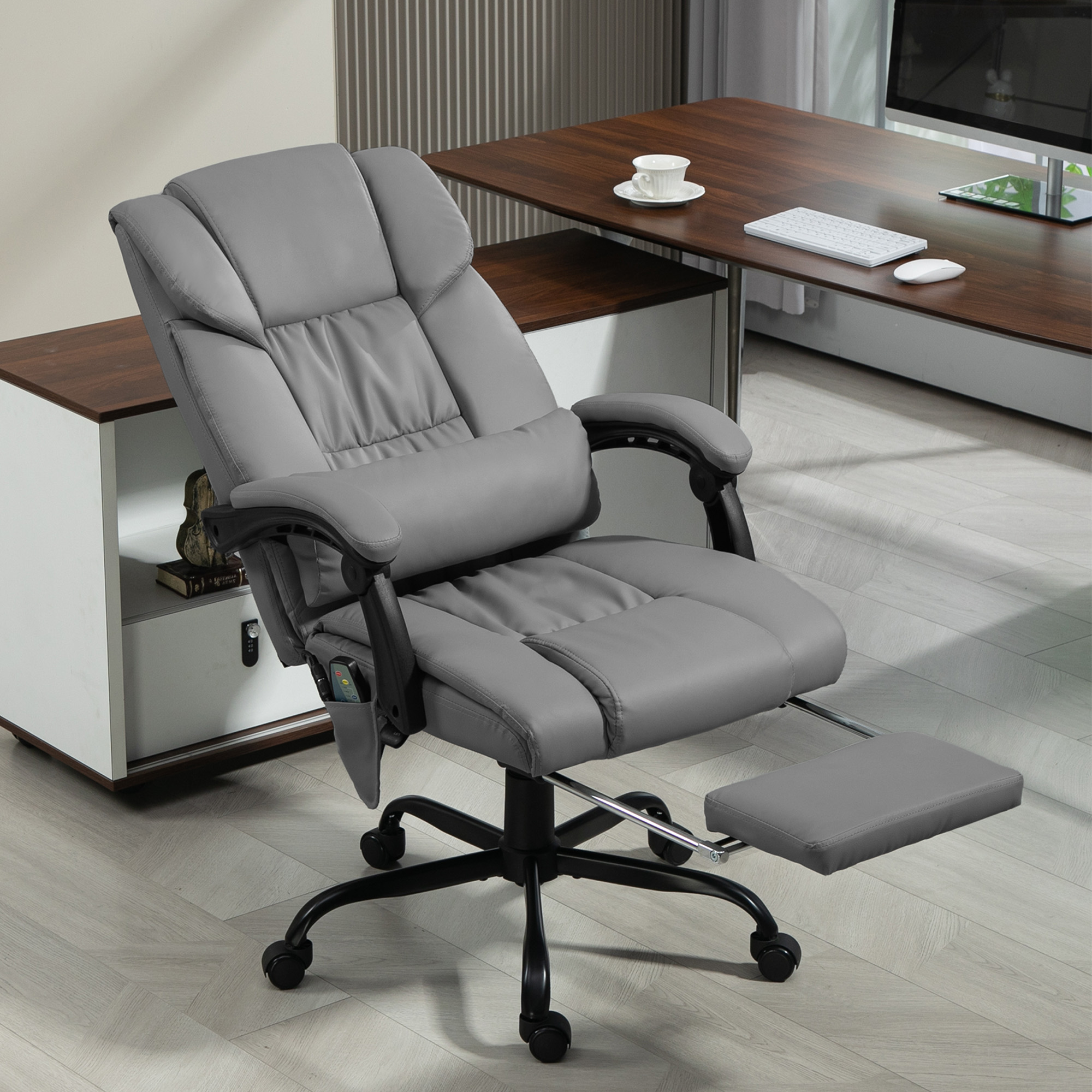 Silla de oficina de cuero gris con reposapiés, base negra y escritorio con computadora.
