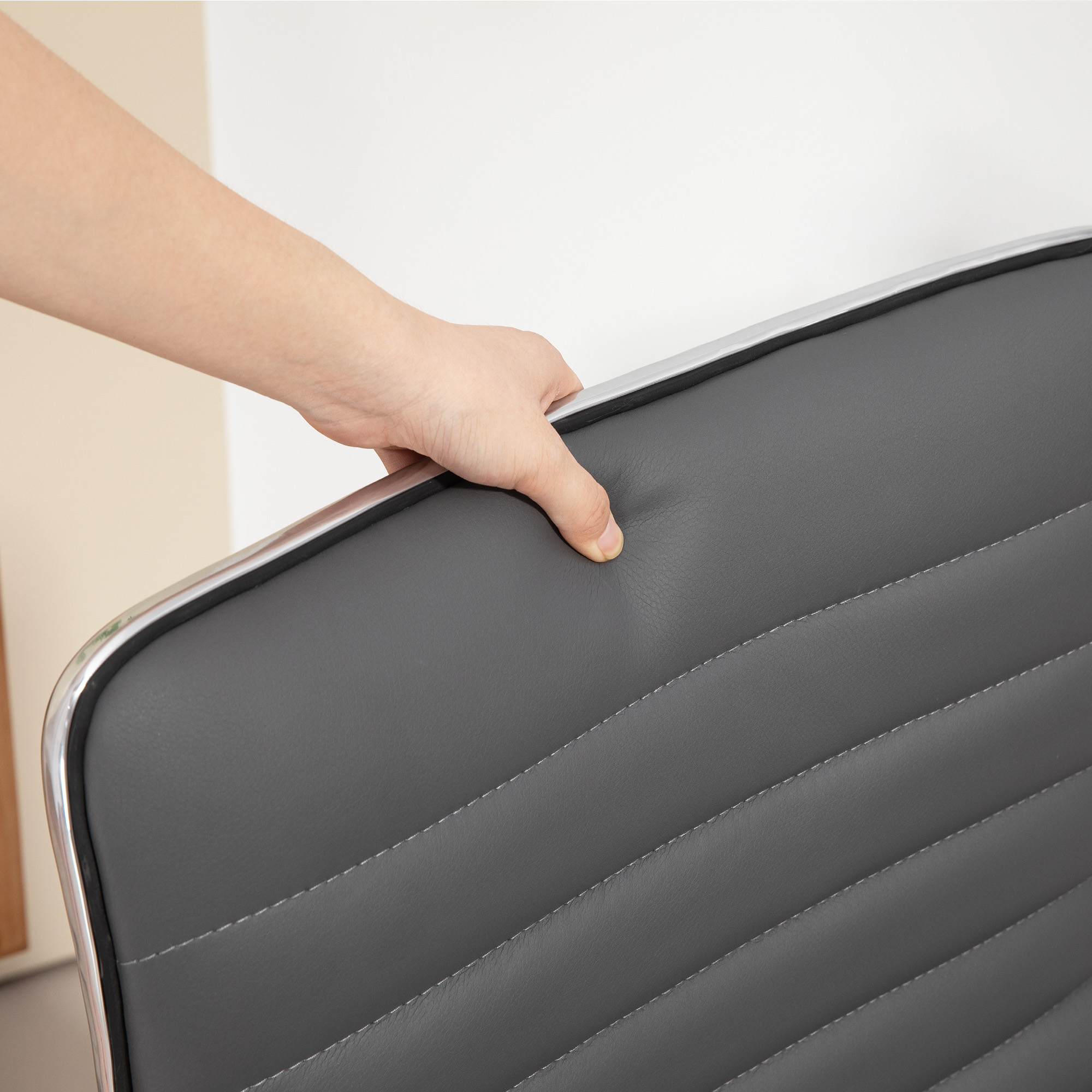 Primo piano di una mano che tocca lo schienale di una sedia in pelle grigia con cuciture.