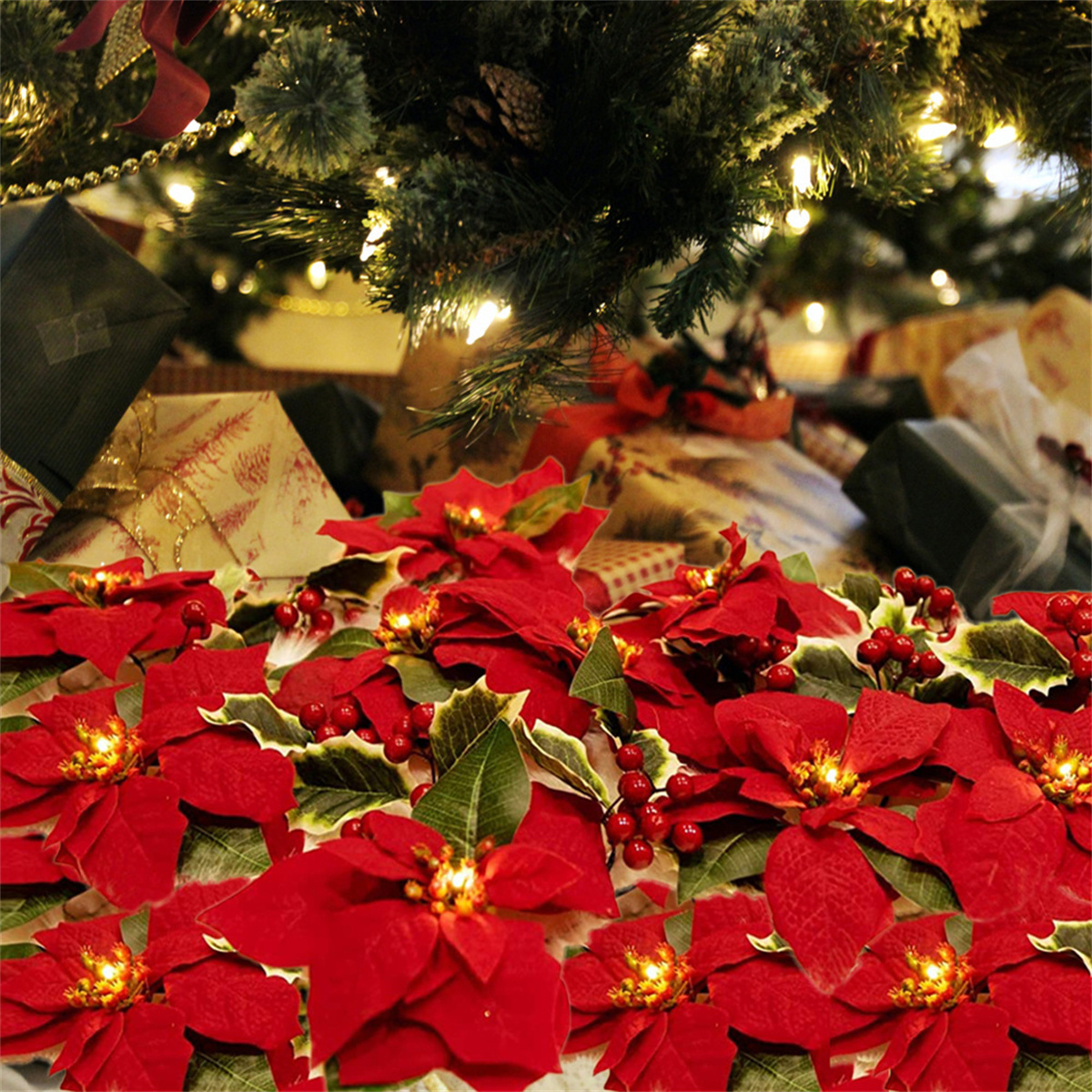 Rote Weihnachtsstern mit grünen Blättern am Fuß eines Weihnachtsbaums, im Hintergrund Geschenke sichtbar.