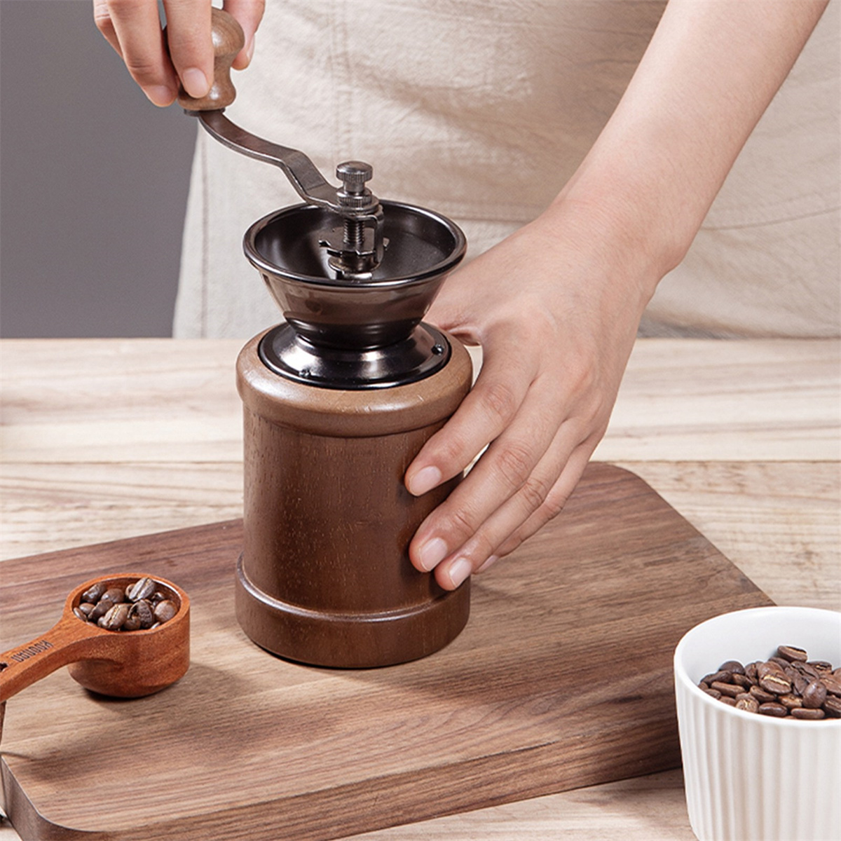 Eine Person, die Kaffeebohnen mit einer Handmühle auf einer Holzoberfläche mahlt.