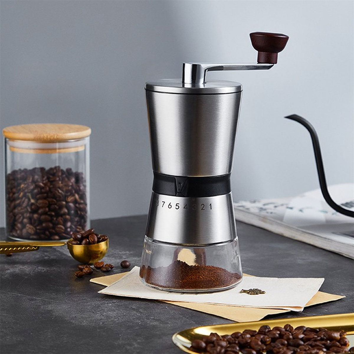 Eine Kaffeemühle aus Edelstahl mit Glasboden. Kaffeebohnen und Kaffeesatz sind auf dem Tisch sichtbar.