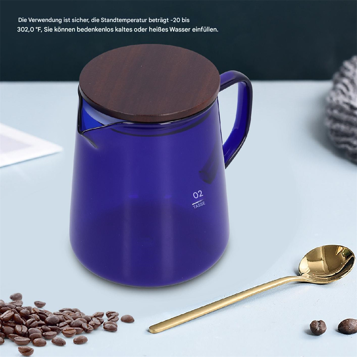 Blaue Glaskaraffe mit Holzdeckel, goldener Löffel und Kaffeebohnen auf Weiß.