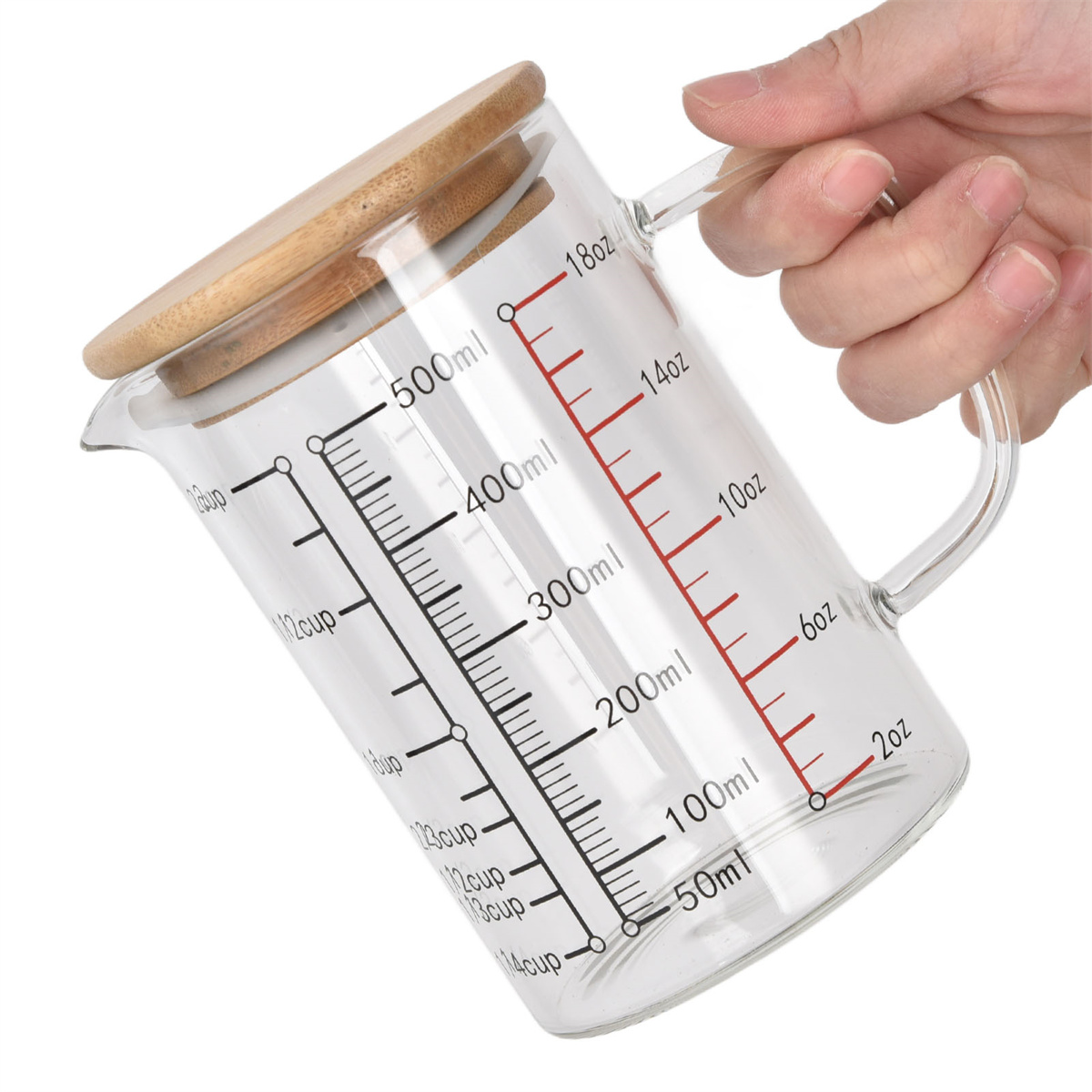 Ein Glas-Messbecher mit Holzdeckel. Er hat Messungen in ml und oz. Wird von einer Hand gehalten.