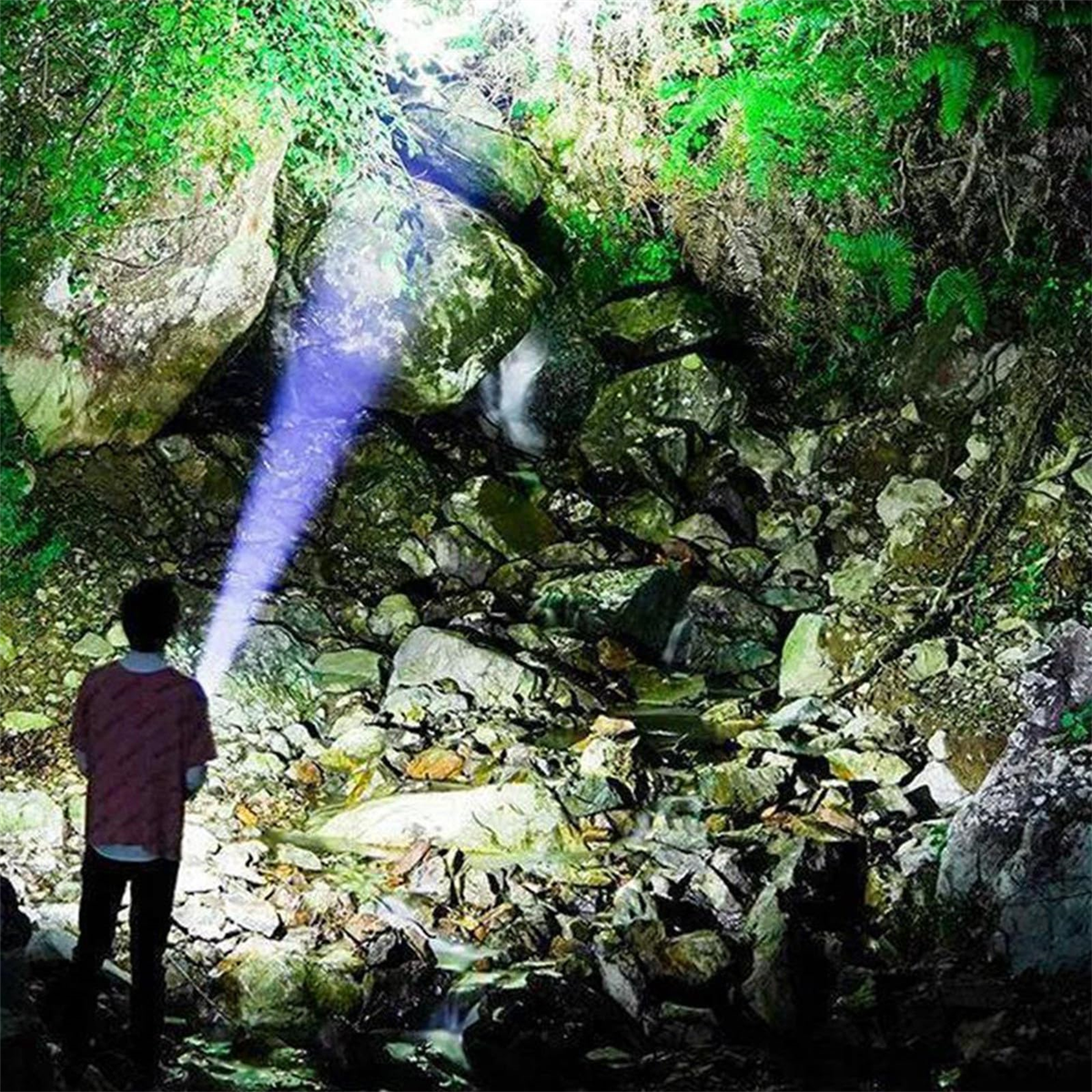 Eine Person, die mit einer Taschenlampe in eine Höhle mit Wasserfall leuchtet.