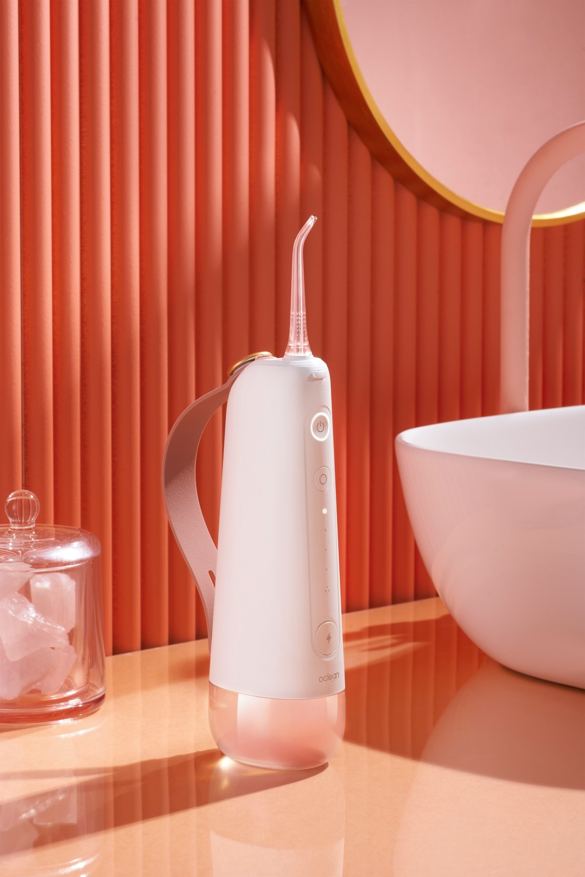 Ein weiß-rosa Munddusche steht auf glänzender Oberfläche, mit Spiegel und Glas im Hintergrund.