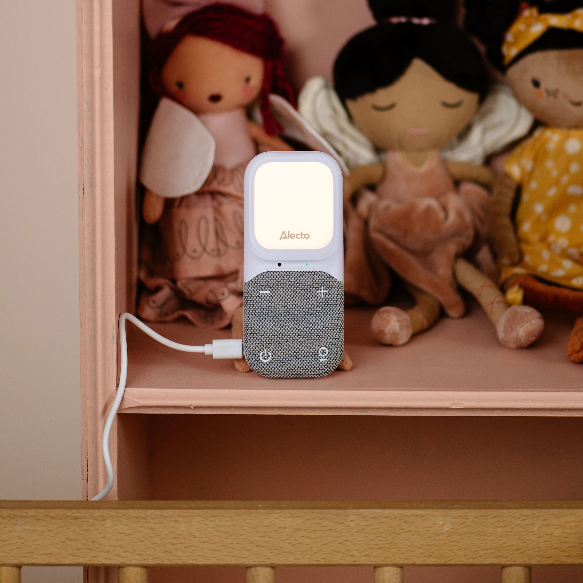 Babyphone auf einer Kommode, mit Puppen im Hintergrund und einem Kinderbett.