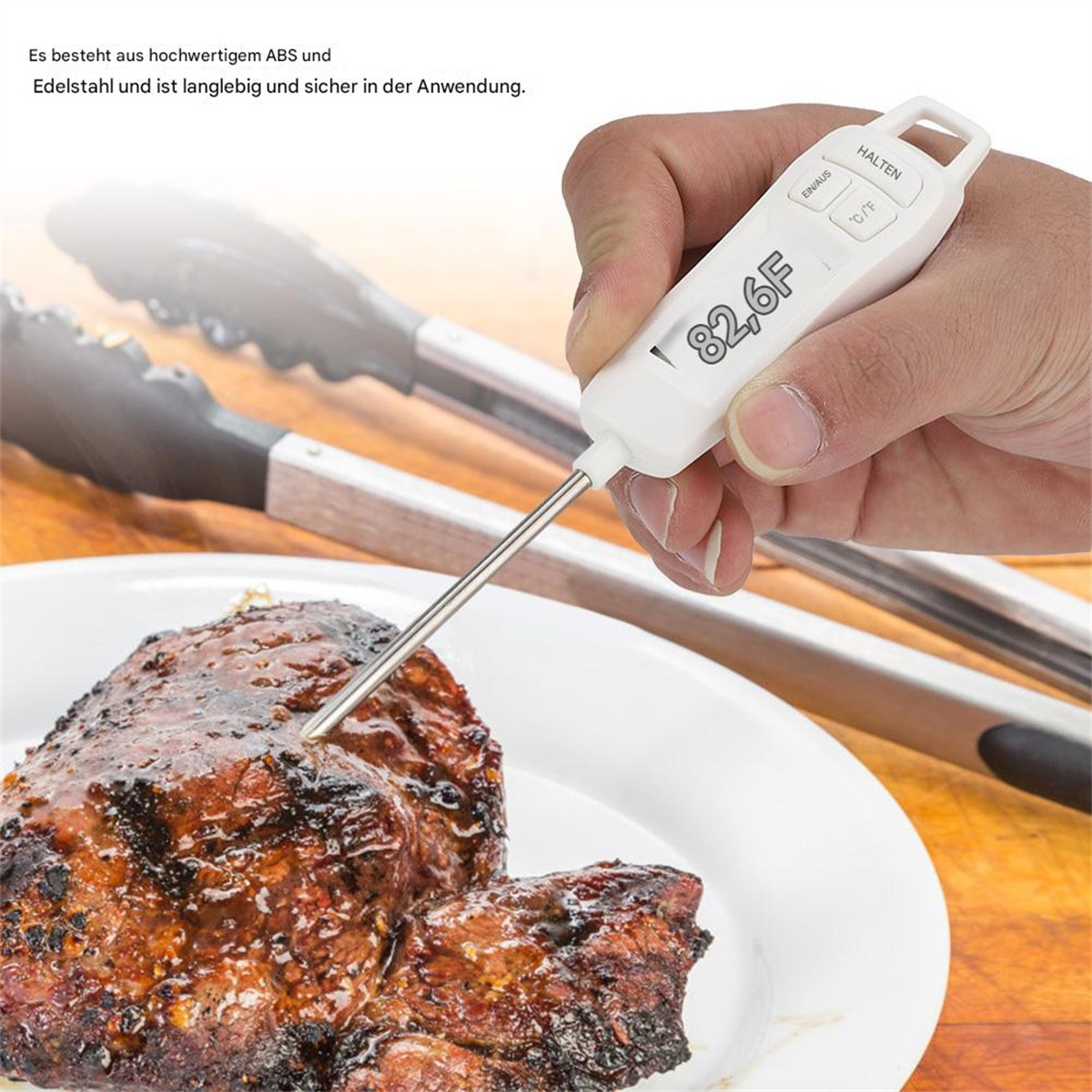 Eine Hand hält ein weißes digitales Thermometer, das die Temperatur von gegrilltem Fleisch auf einem Teller misst.