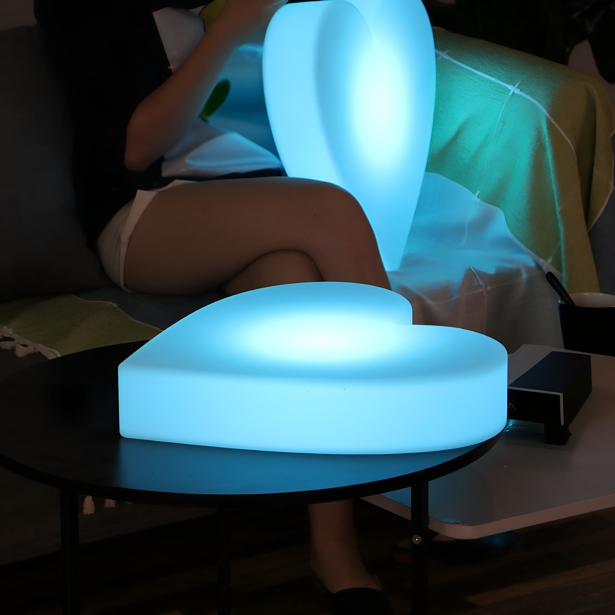 Eine Person sitzt in der Nähe von herzförmigen, blau leuchtenden Lichtern. Eines steht auf einem Tisch.