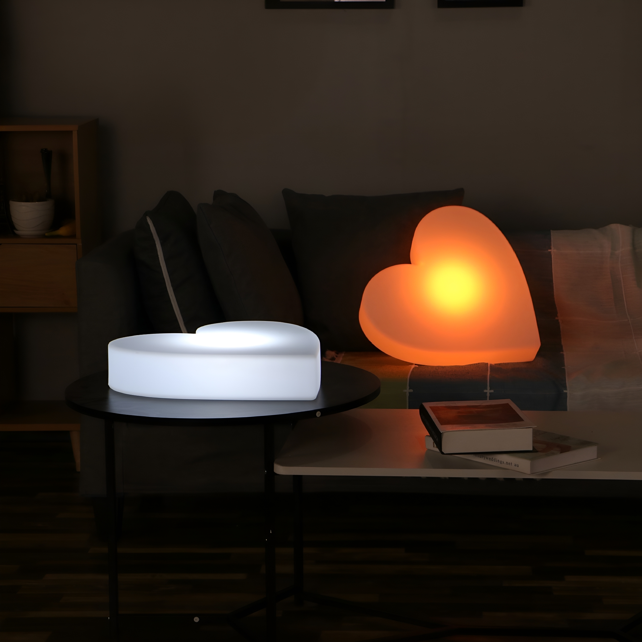 Wohnzimmer mit zwei herzförmigen Lampen. Eine ist weiß, eine ist orange. Dunkler Hintergrund.