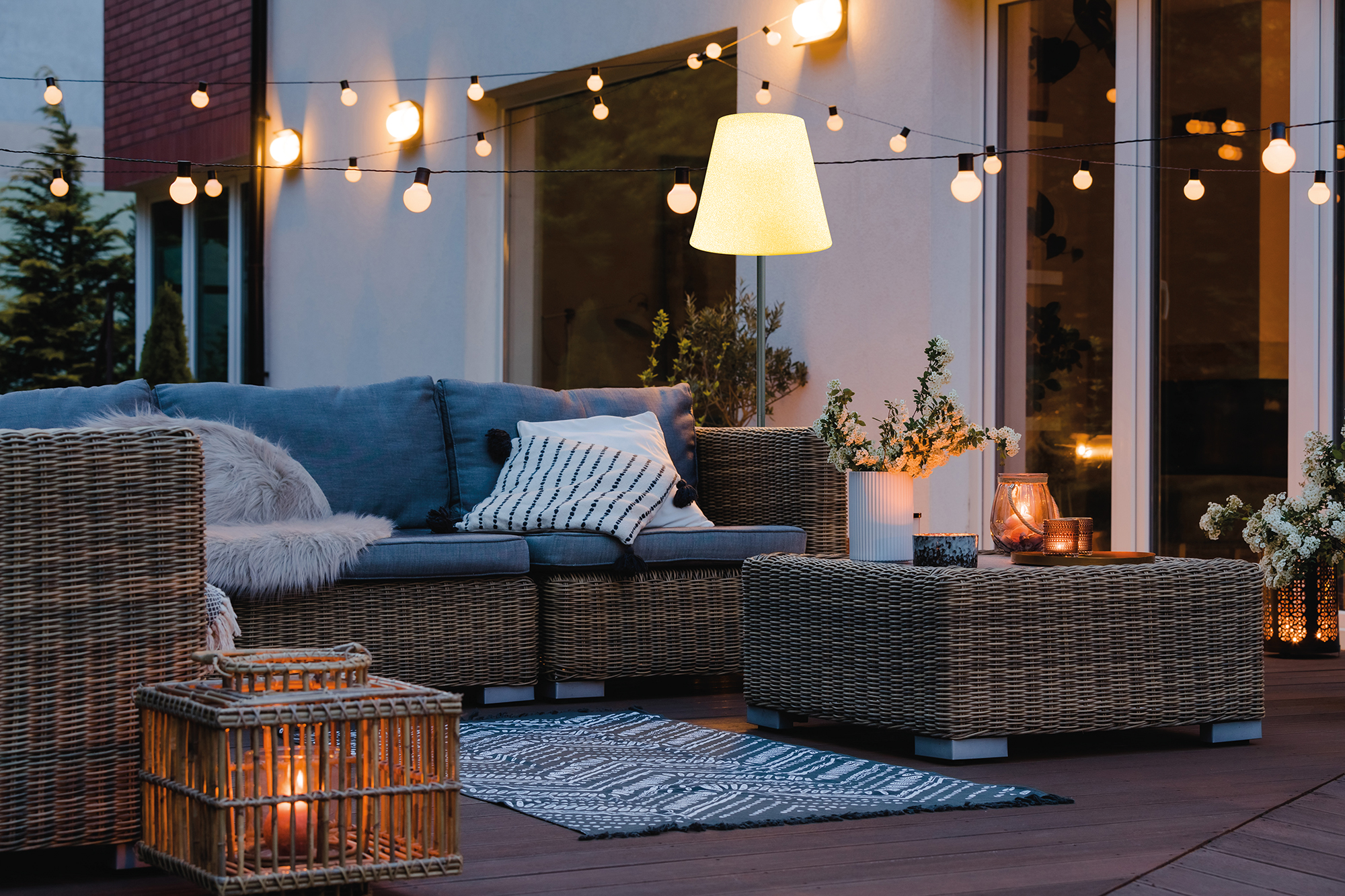 Eine Außenterrasse mit Sofa, Tisch und Lichterketten. Ein Teppich und Laternen liegen auf dem Boden.