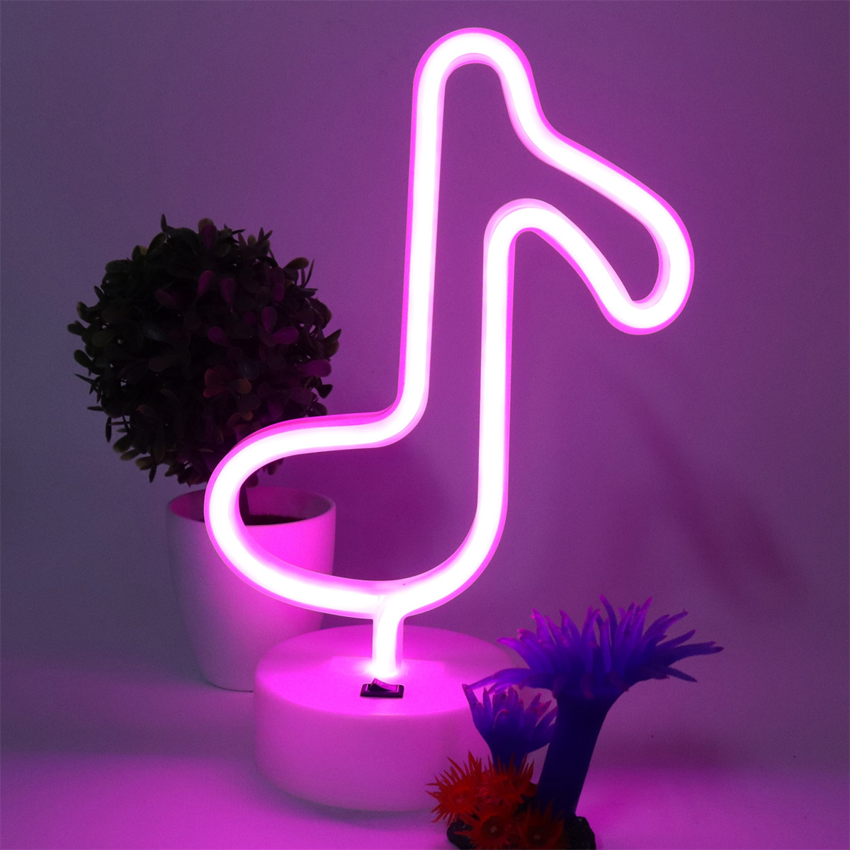 Neonrosa Musiknote. Sie steht auf weißem Sockel, mit einer kleinen Pflanze und einer Blume.