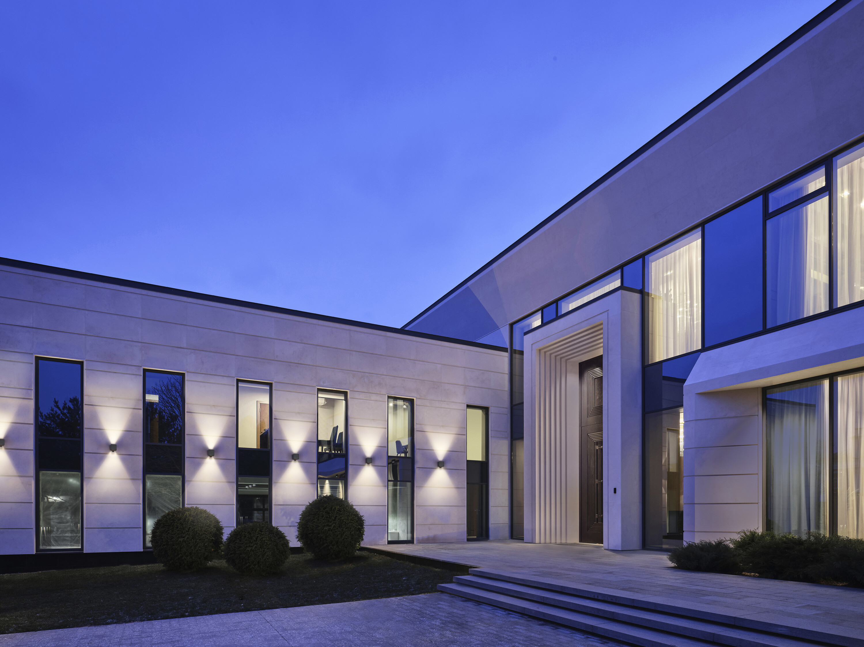 Modernes Gebäude im Zwielicht. Helle Fassade, große Fenster und architektonische Beleuchtung.
