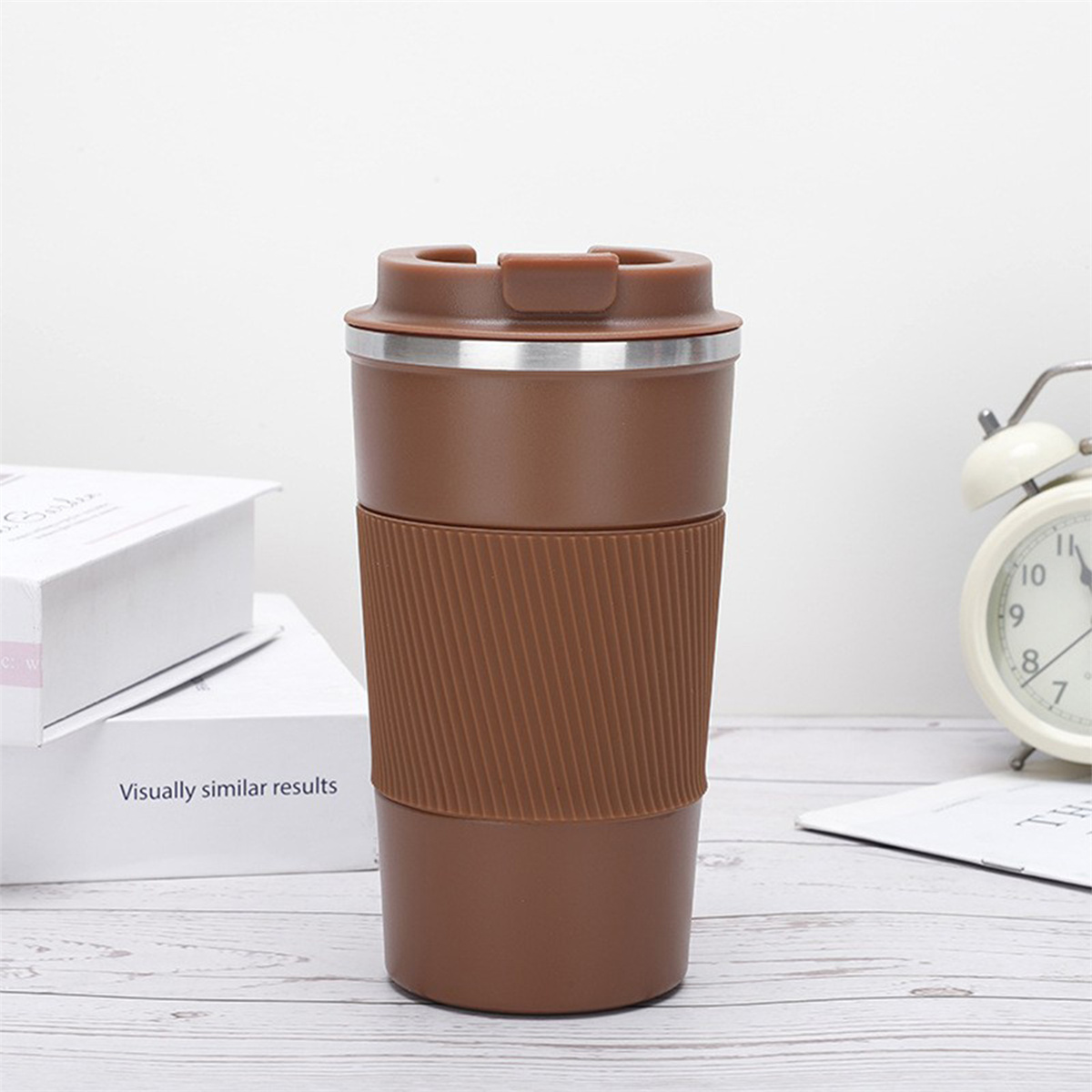 Ein brauner Reisebecher mit silbernem Rand und geripptem Griff, mit weißem Hintergrund.