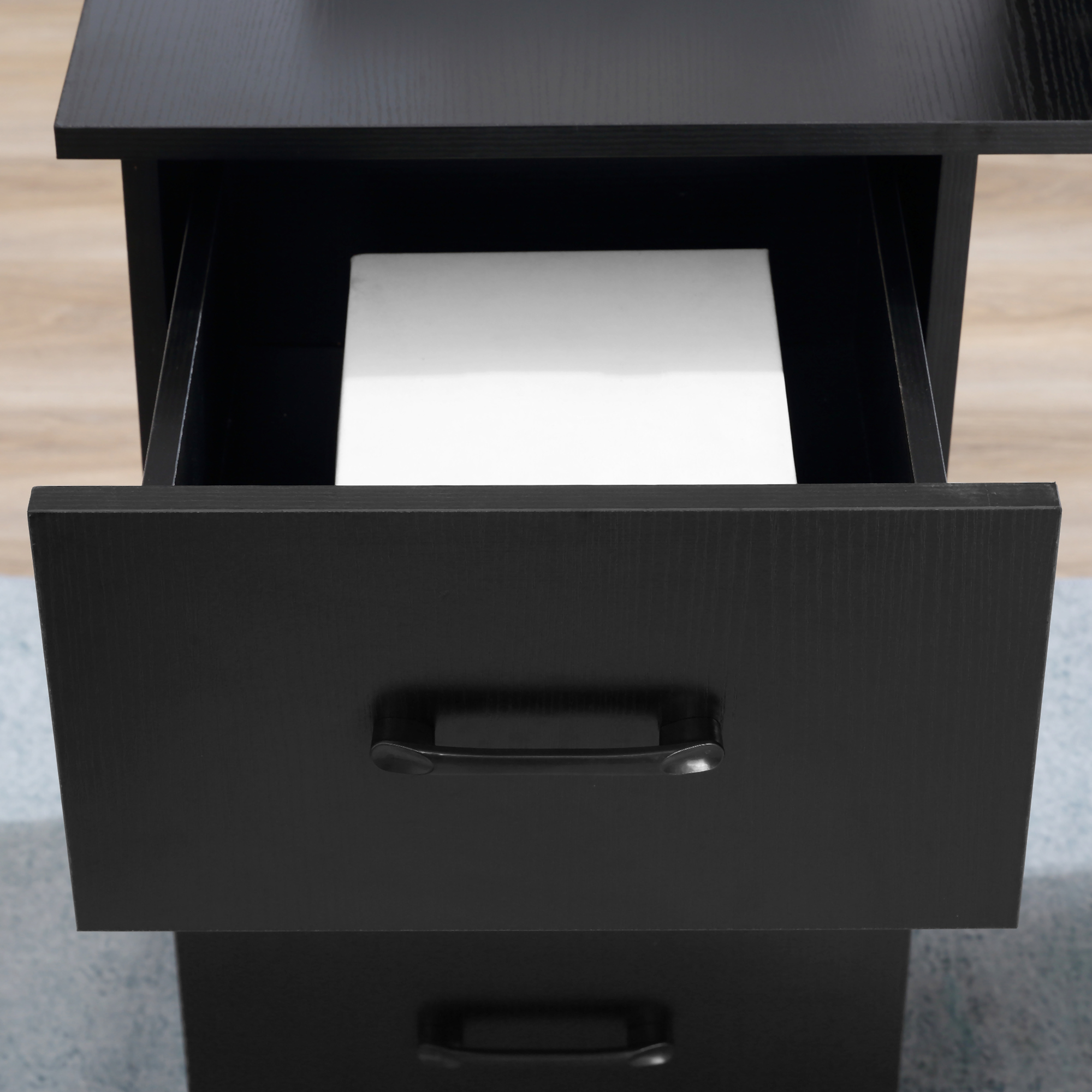 Primo piano di cassetti neri. Il cassetto superiore è aperto e rivela un oggetto bianco. Le maniglie sono nere.