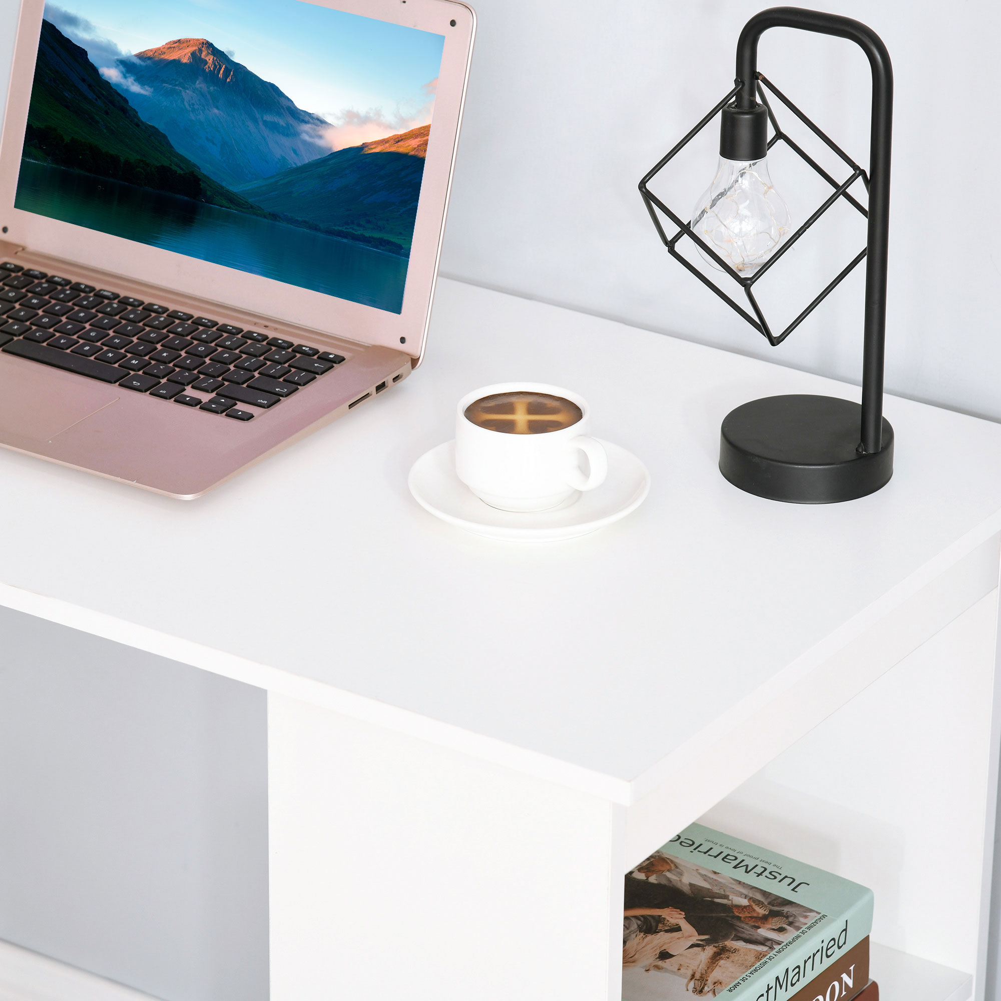 Scrivania bianca con laptop, caffè e lampada. Libri e decorazioni sopra.