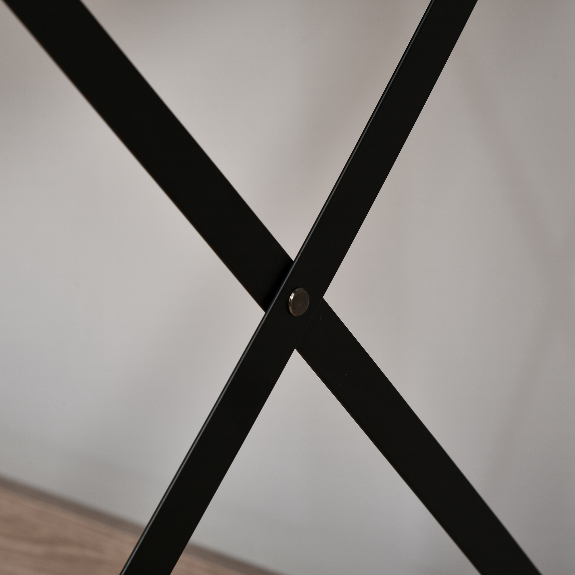 Un primo piano mostra le gambe in metallo nero di un tavolo, con un design a X e un rivetto argentato.