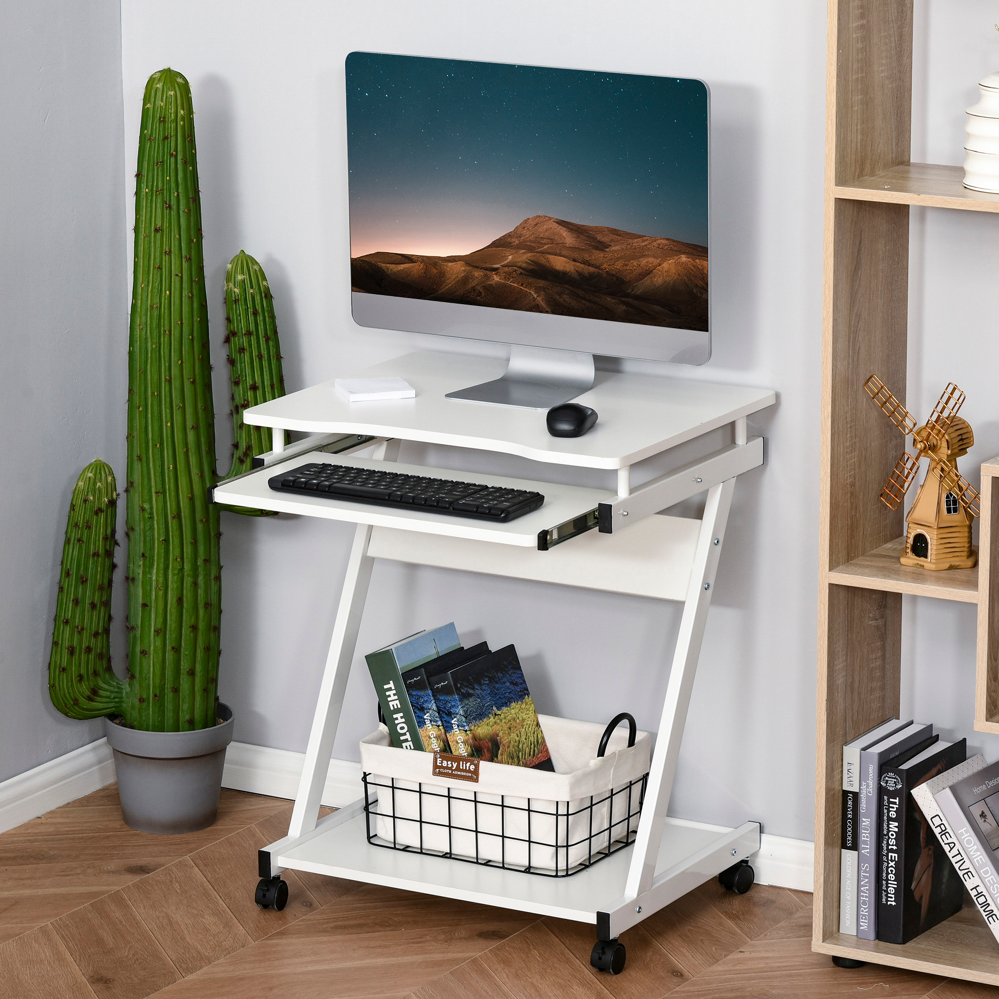 Scrivania bianca con monitor, tastiera e libri. Cactus e scaffale in legno sullo sfondo.