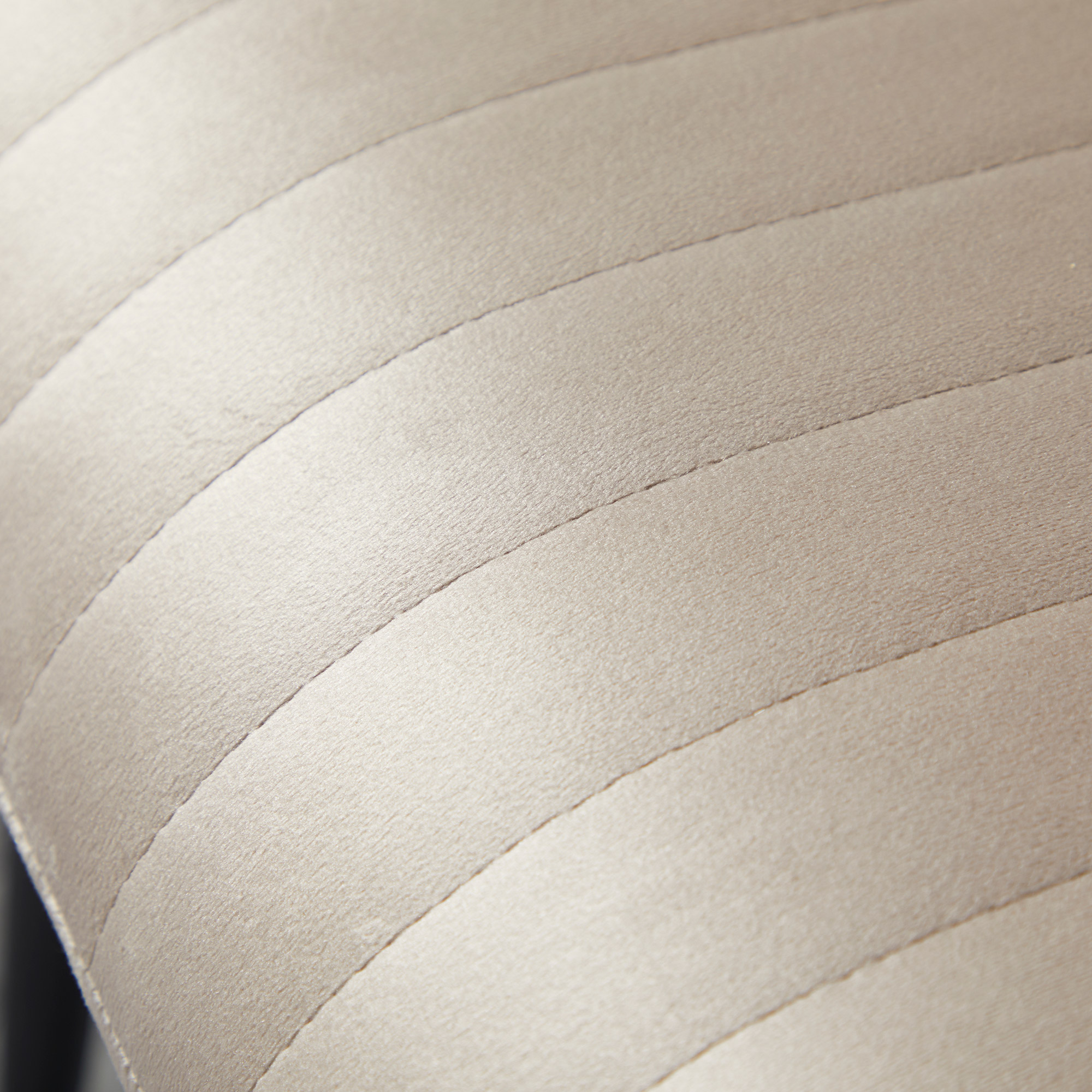 Primo piano di un sedile beige chiaro imbottito con linee orizzontali cucite.
