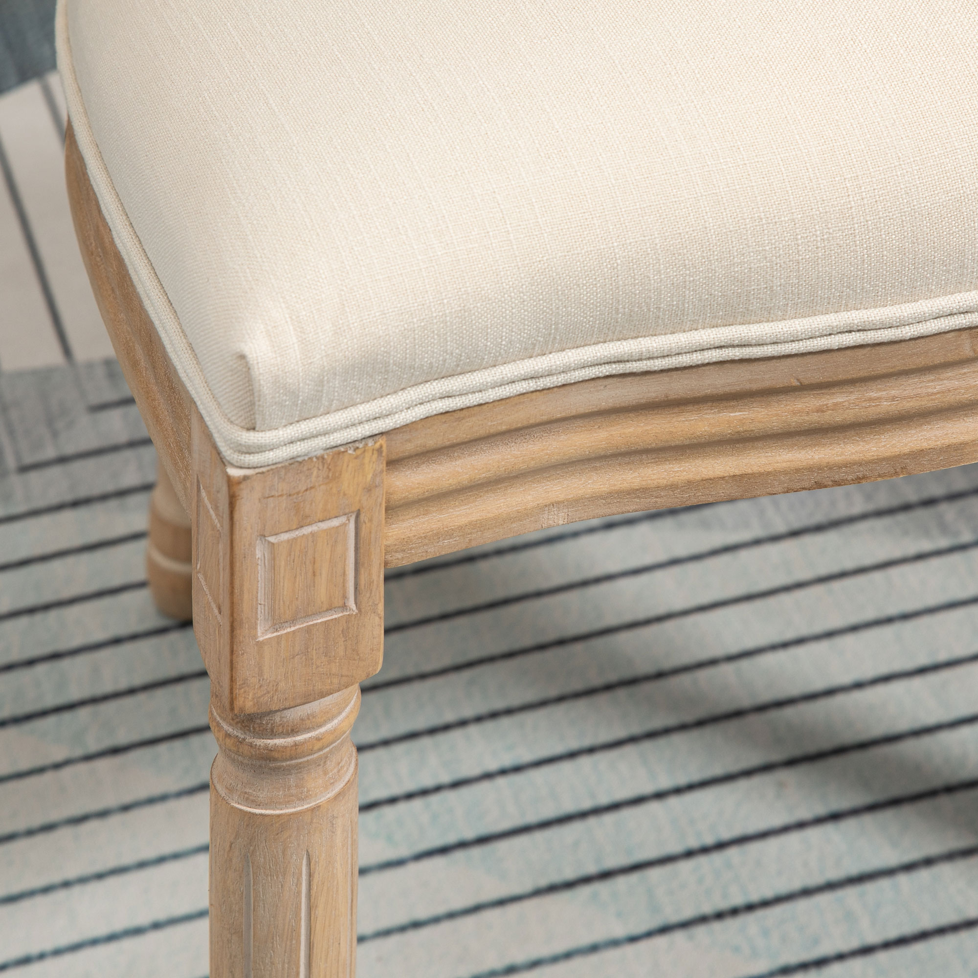 Primo piano della seduta di una sedia con tessuto beige. Il telaio in legno ha un bordo decorativo.