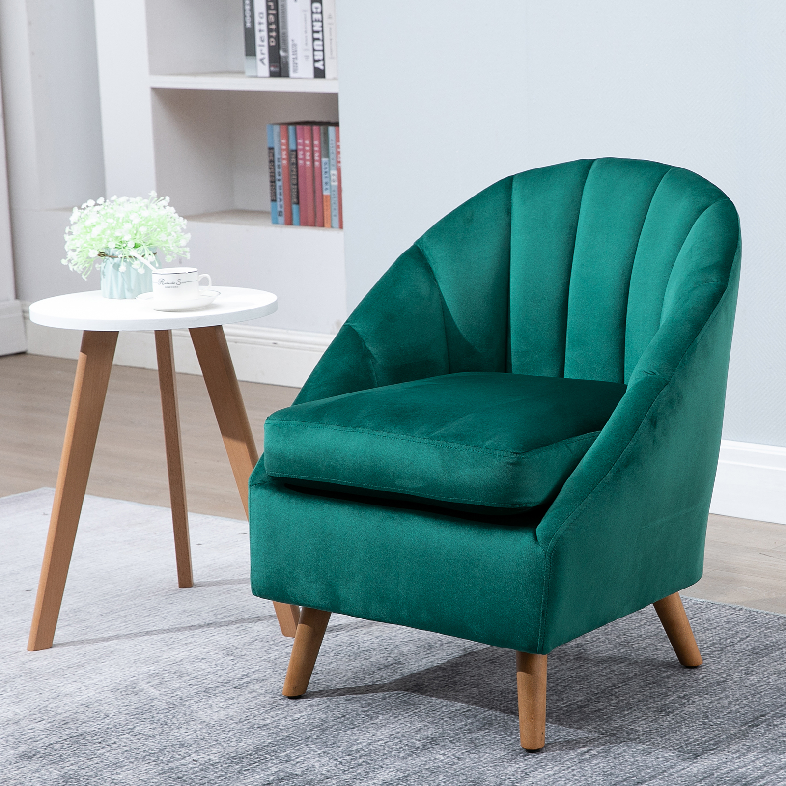 Una poltrona verde con un tavolino bianco, una piccola pianta e una tazza sopra. Tappeto morbido e libri sullo sfondo.