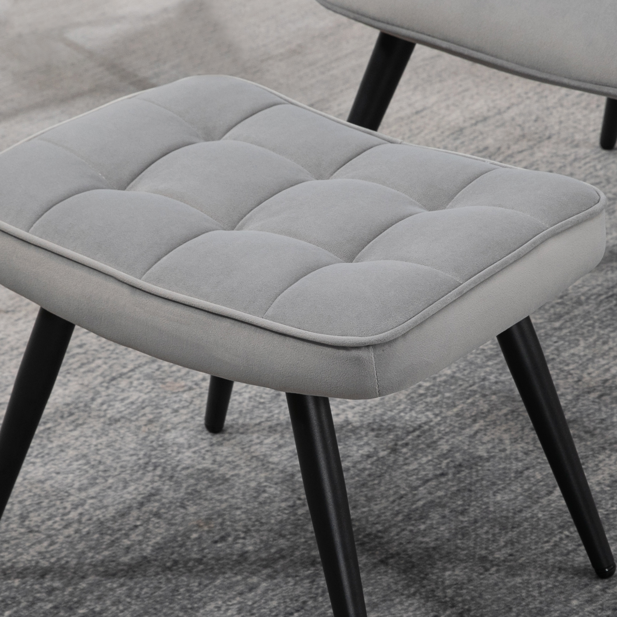 Ein grau gepolsterter Hocker mit schwarzen Metallbeinen. Der Sitz hat ein gestepptes Design.