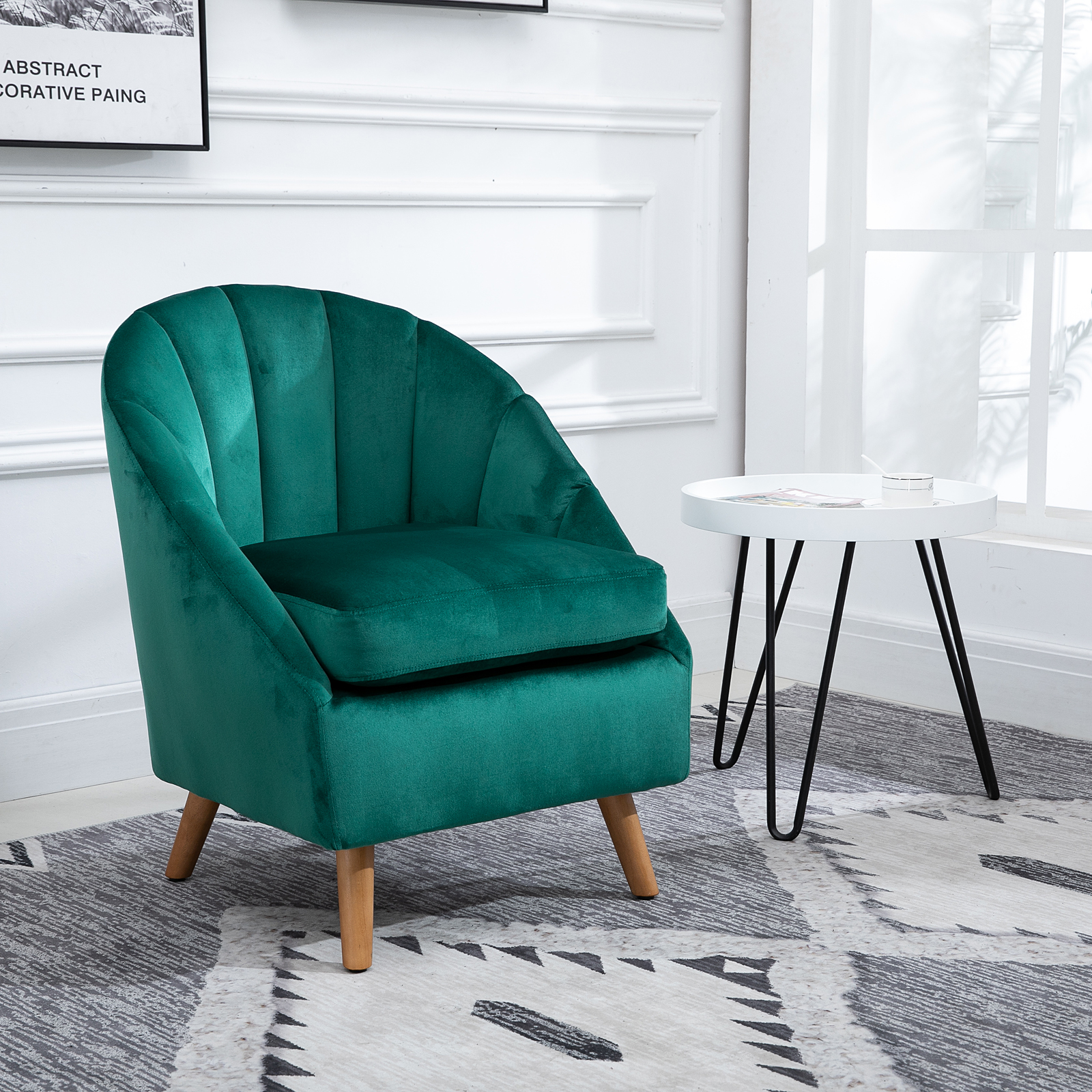 Una sedia in velluto verde con gambe in legno accanto a un tavolino bianco.