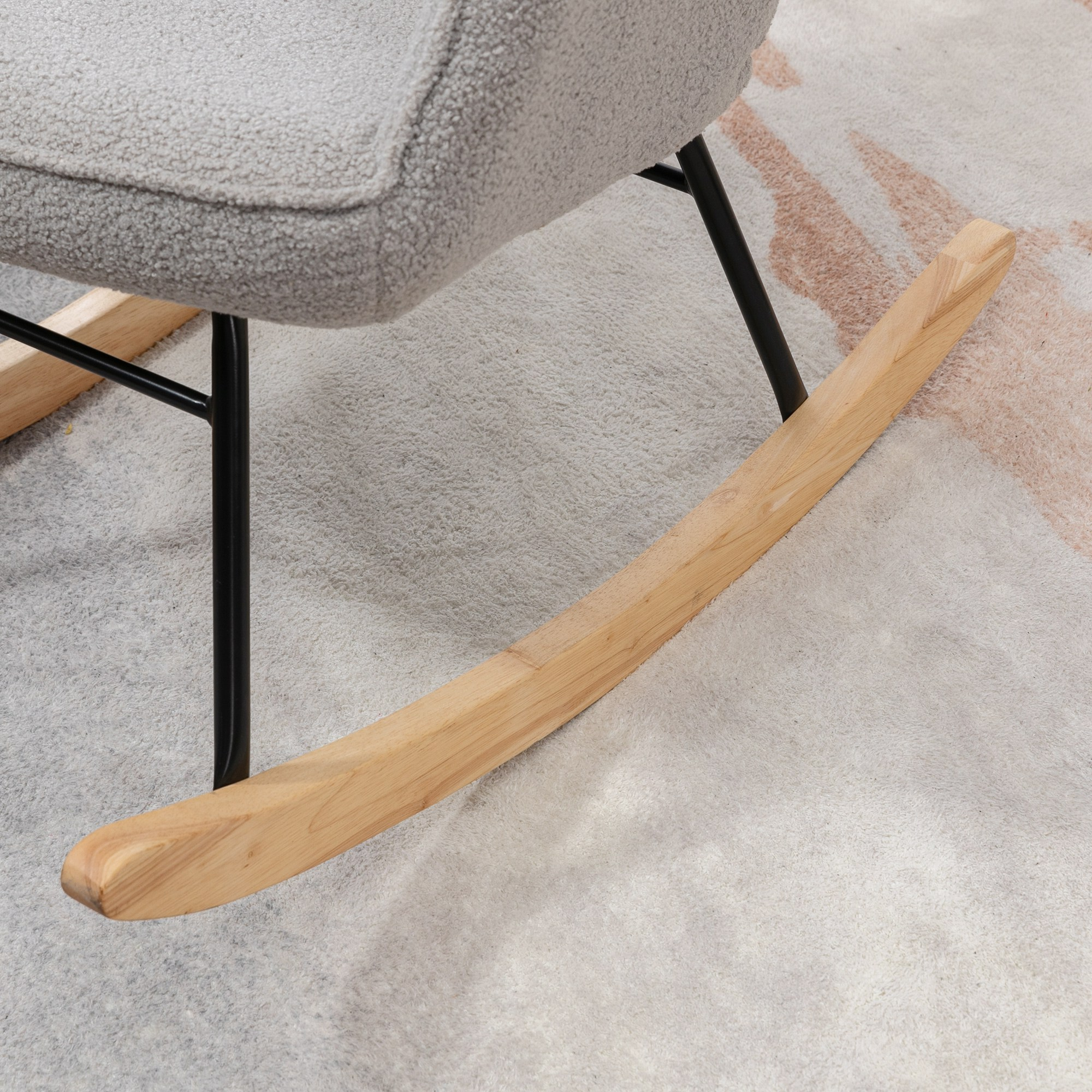 Pattino di sedia a dondolo in legno su un tappeto fantasia. Tonalità rosa chiaro e bianco.