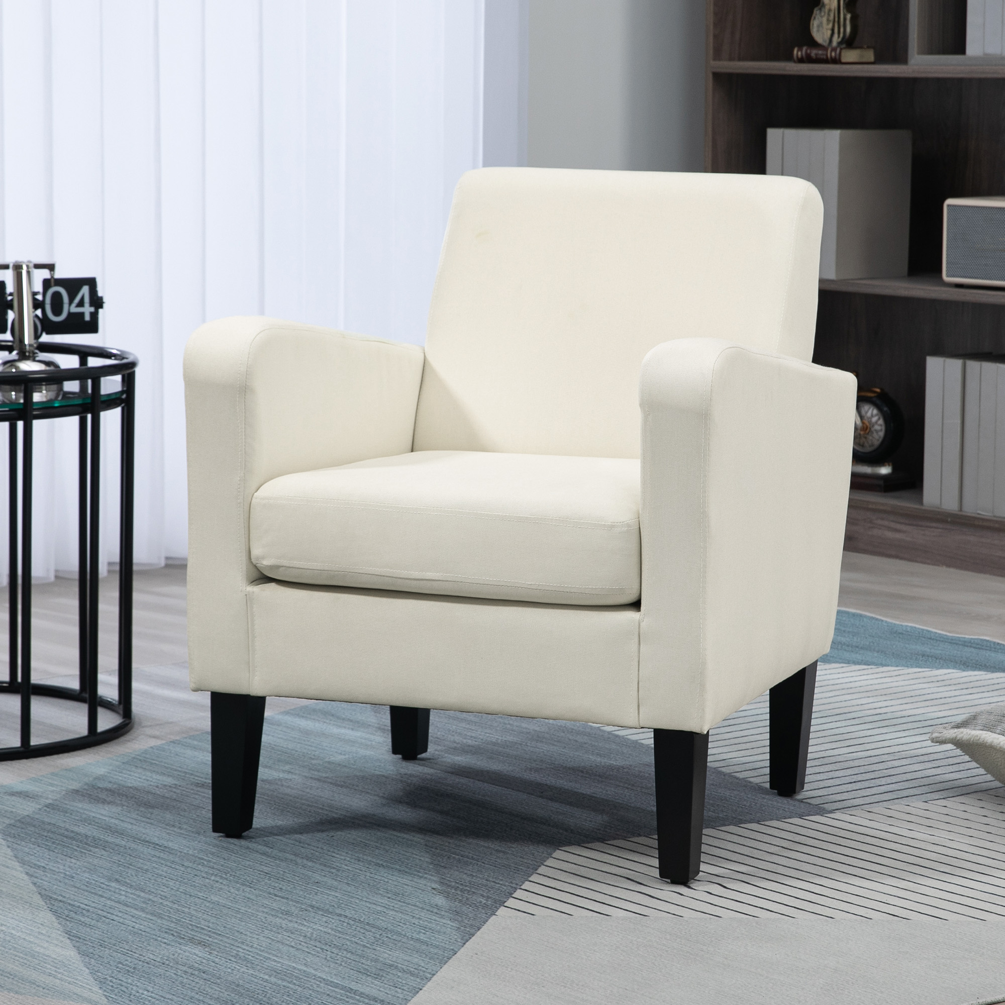 Poltrona color crema con gambe nere. Tavolo e libreria sullo sfondo.