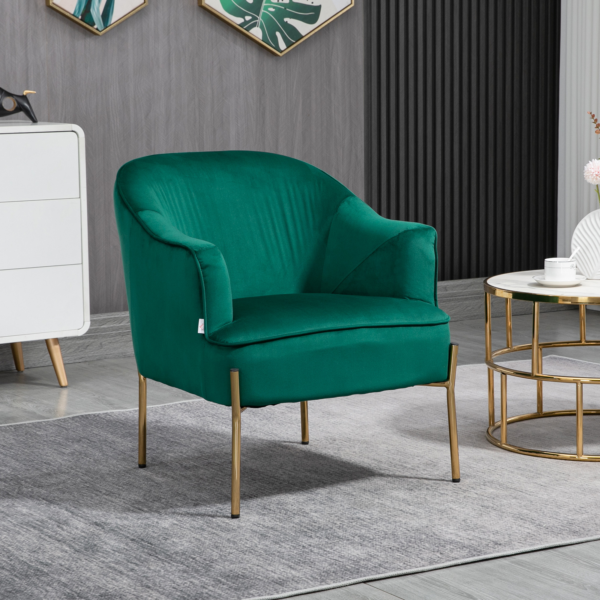 Poltrona verde in velluto con gambe dorate su tappeto grigio. Credenza bianca e tavolino dorato sullo sfondo.