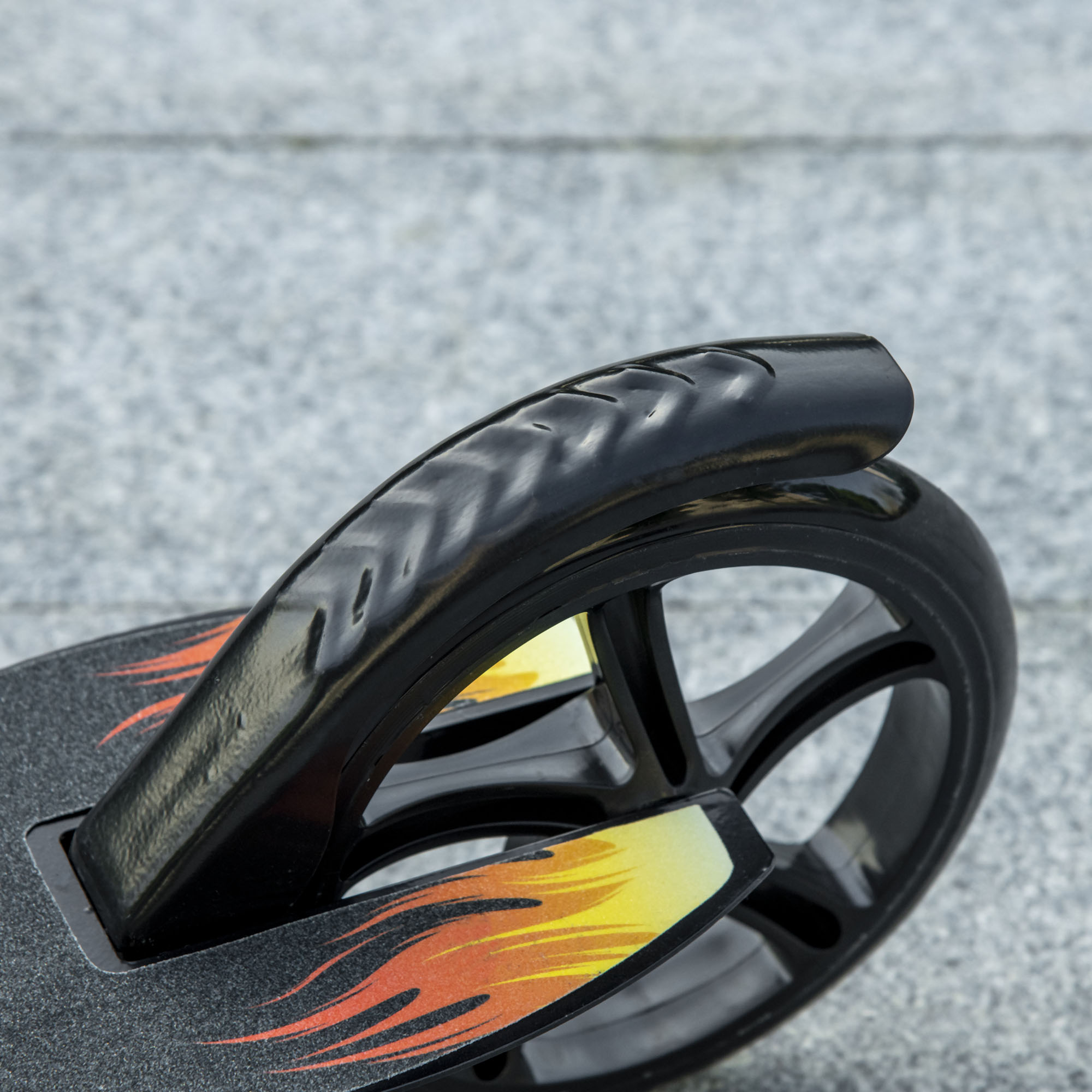 Primo piano di una ruota di scooter nera con un design a fiamma. La ruota è su una superficie grigia.