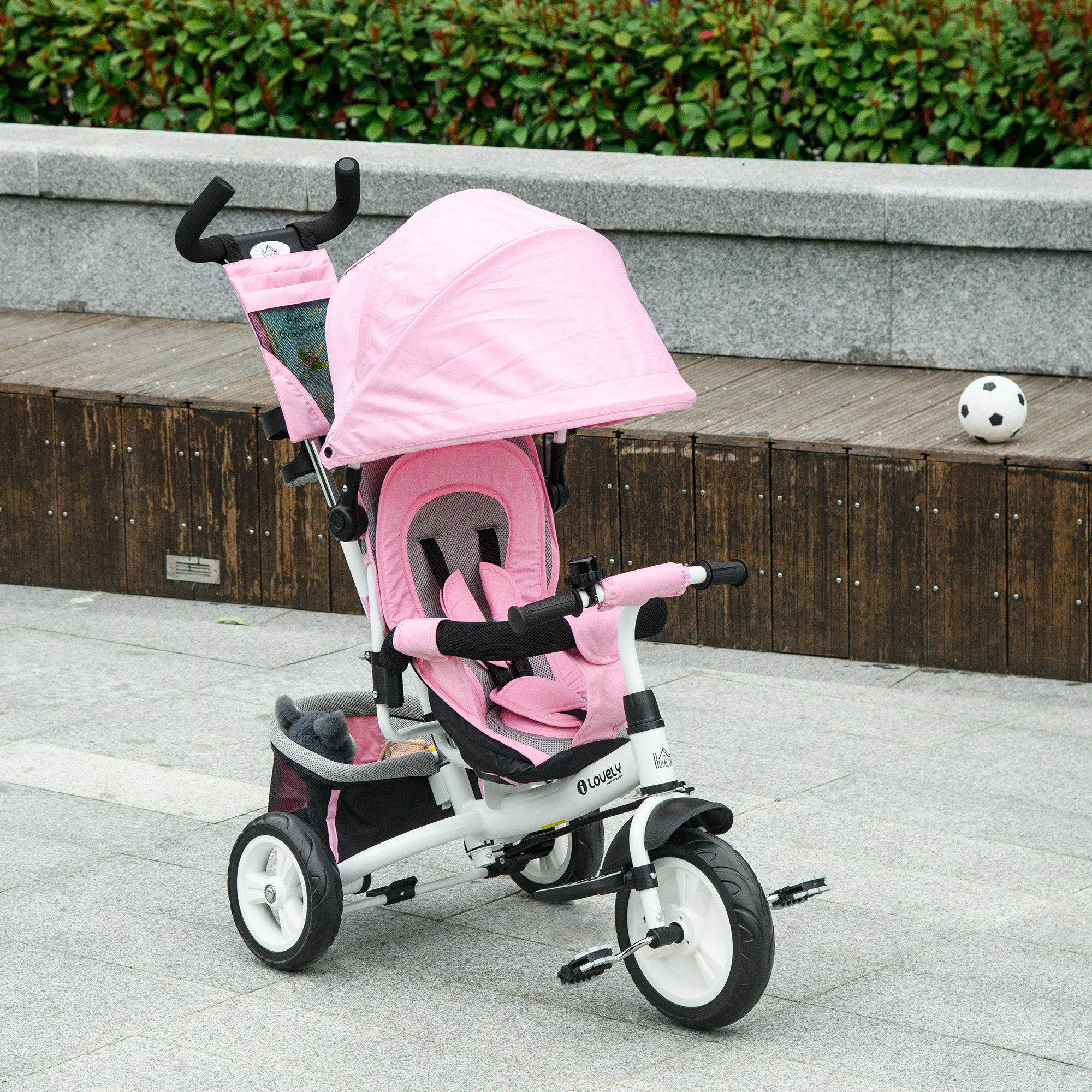 Un passeggino rosa con un cestino nero. Ha una capote rosa ed è su un marciapiede grigio.