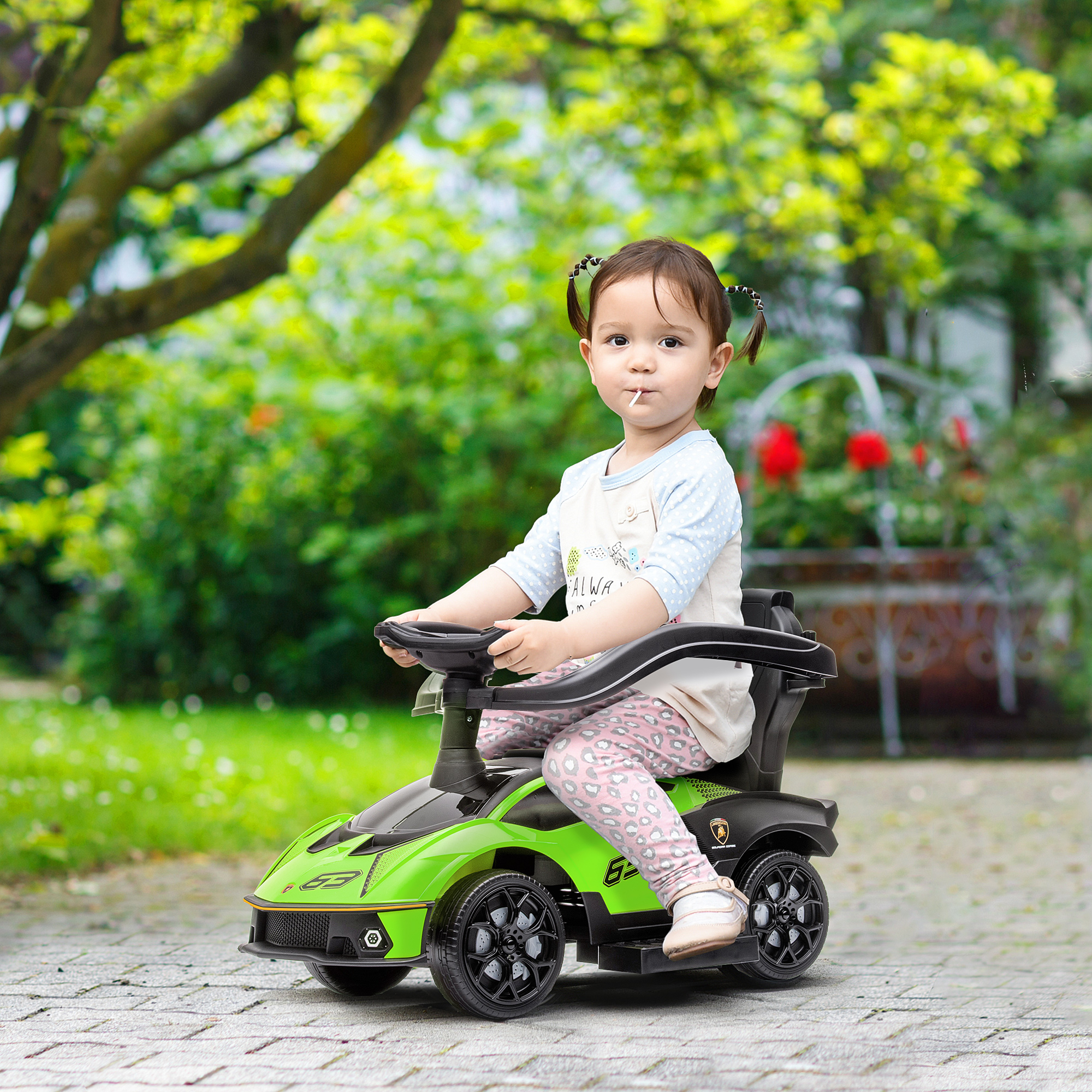 Un bambino è seduto in un'auto giocattolo verde, sorridente, su un sentiero lastricato. L'auto ha ruote nere.