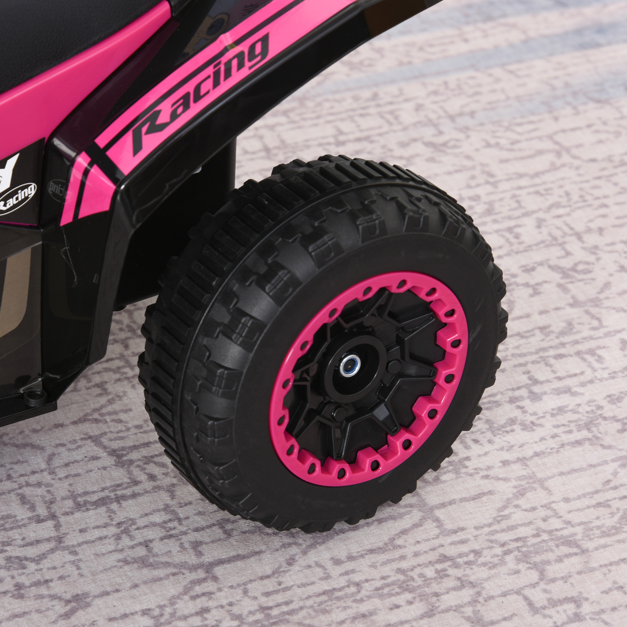 Primo piano di una ruota di un'auto giocattolo, cerchio rosa, pneumatico nero, su una superficie decorata.