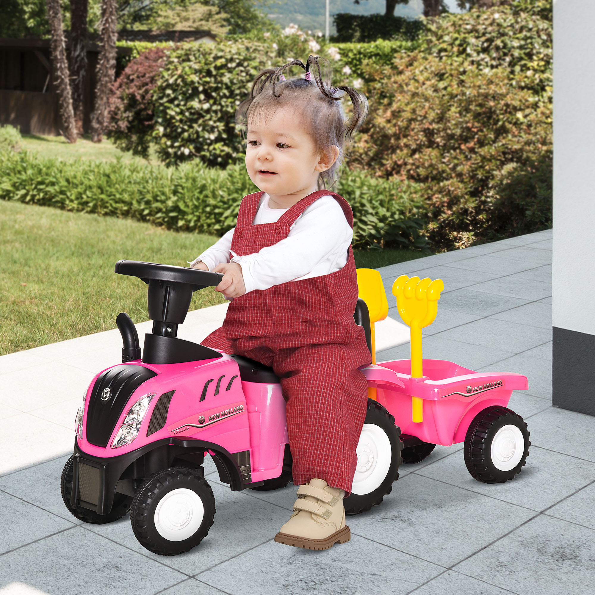 Bebé con mono rojo en un tractor de juguete rosa con remolque amarillo.