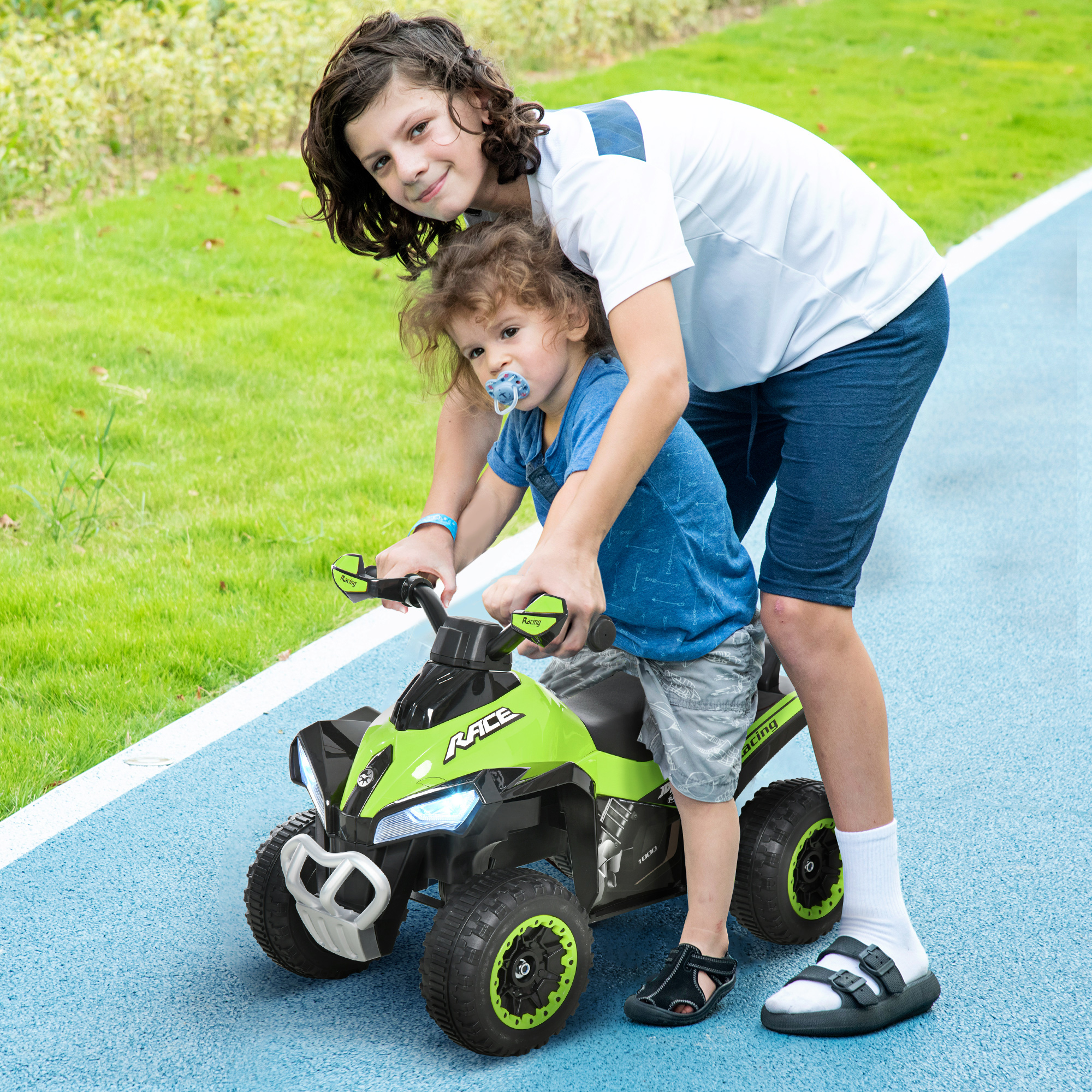 Dos niños con un juguete ATV verde y negro. Uno conduce, el otro apoya.