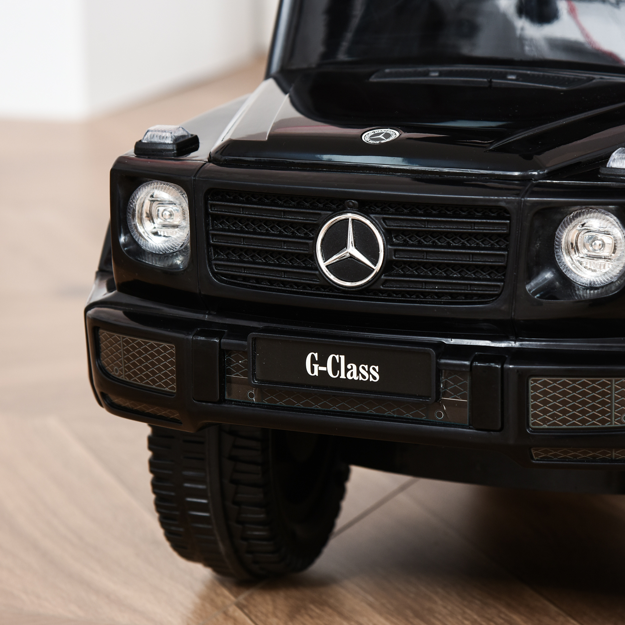 Primo piano della parte anteriore di un'auto giocattolo nera. Ha il logo Mercedes e la scritta Classe G.