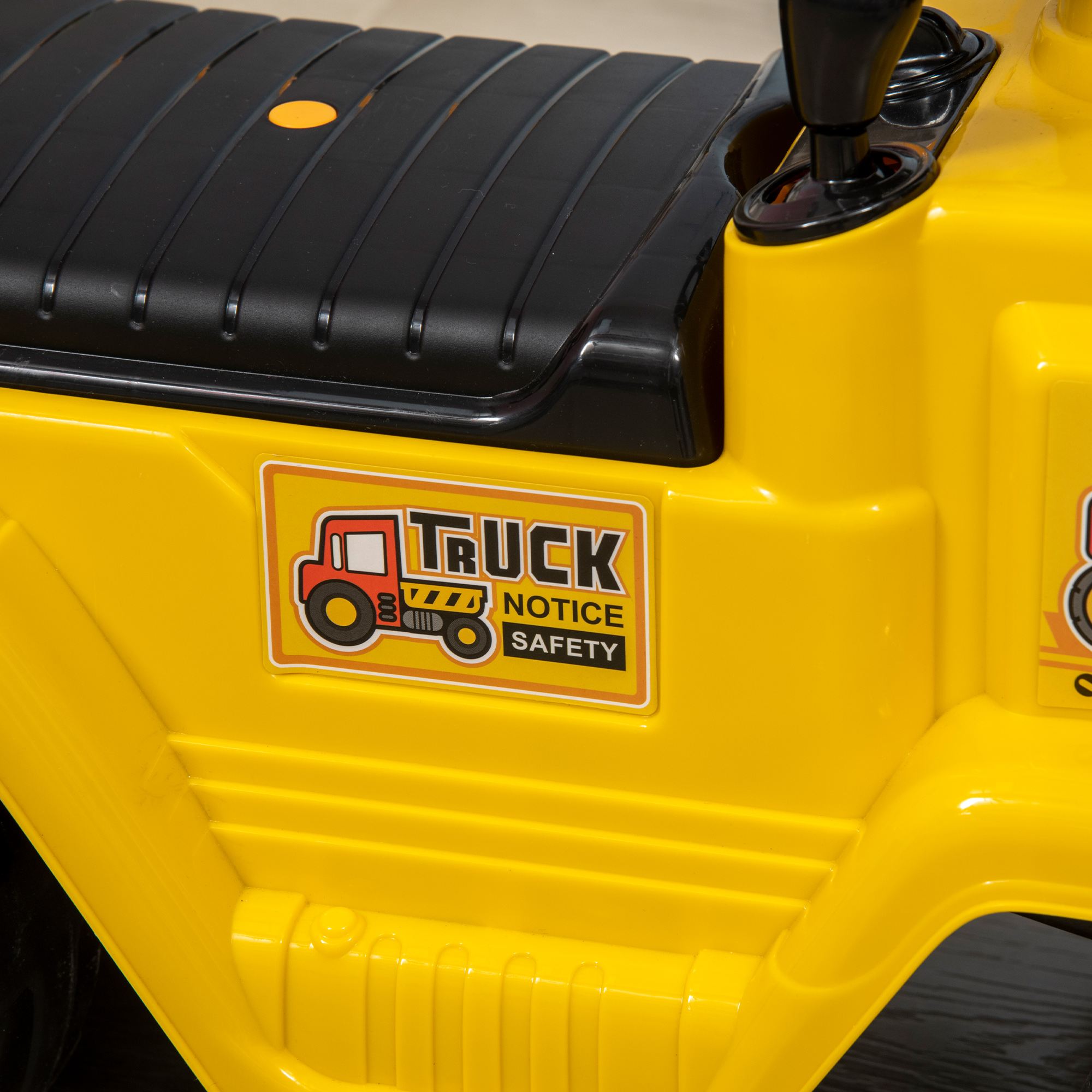 Primo piano di un camion giocattolo giallo con un adesivo che dice “TRUCK NOTICE SAFETY”. Dettagli neri.