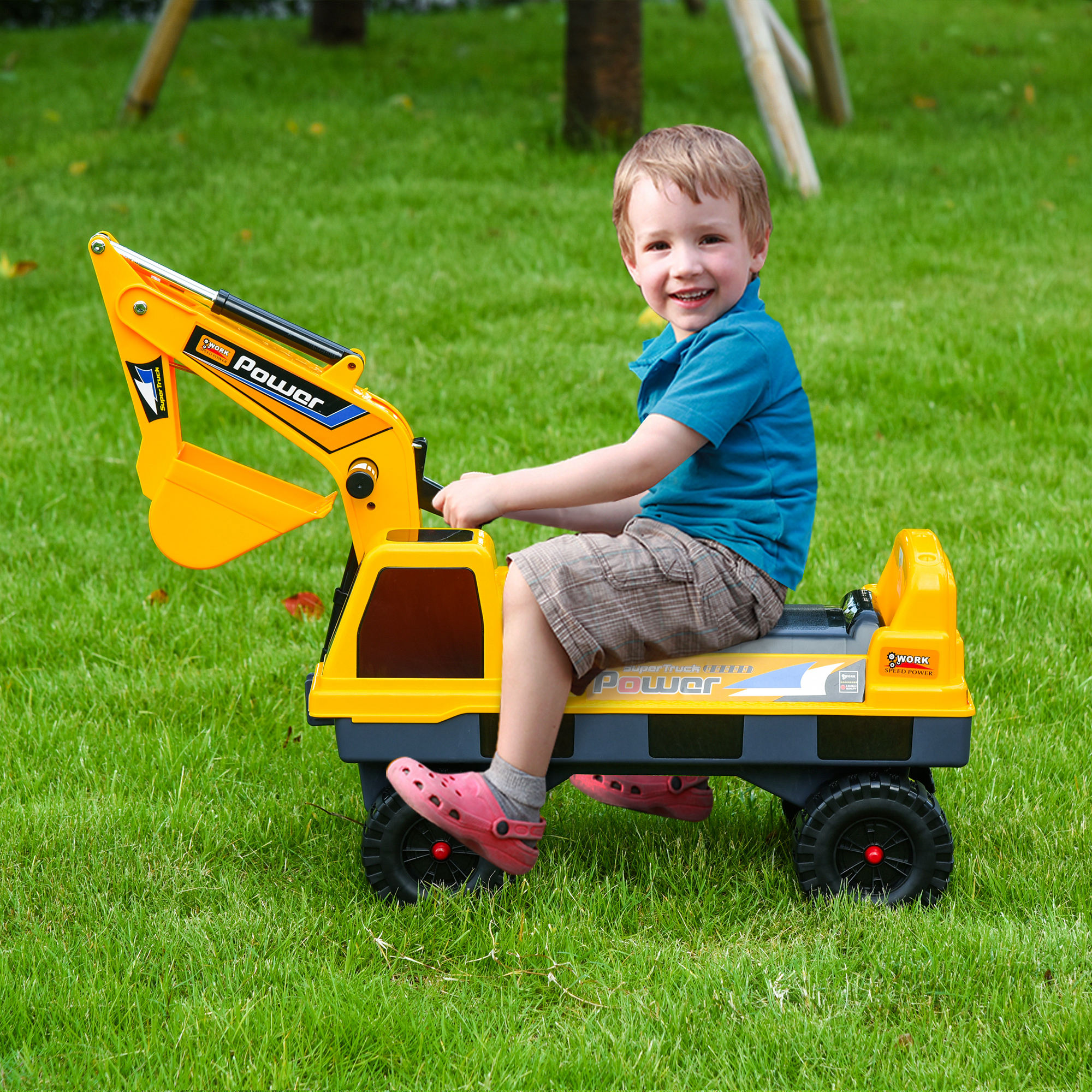 Bambino su un giocattolo escavatore giallo. Sfondo di erba verde, sorridente, con scarpe rosa.