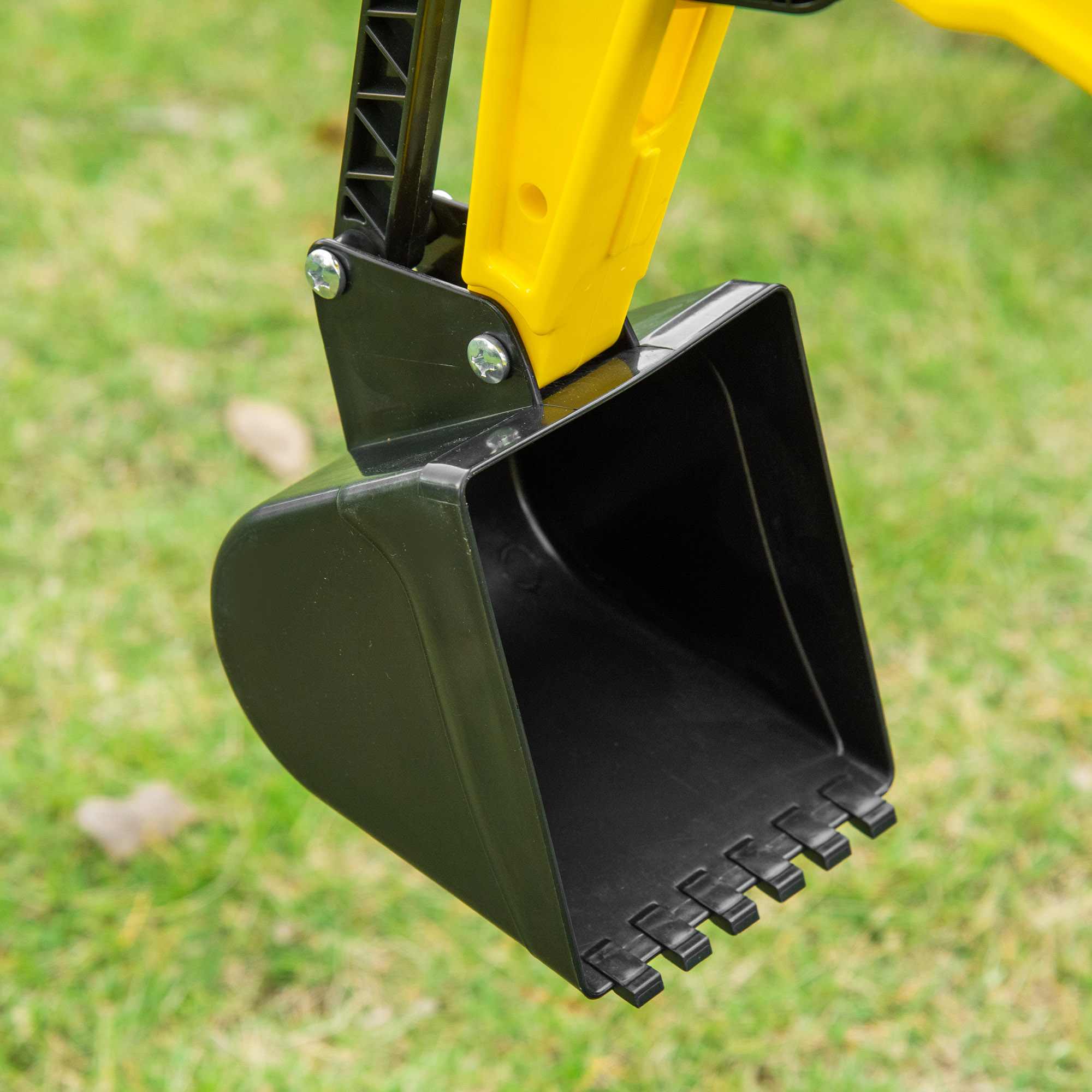 Primo piano di una benna nera di un escavatore. Braccio giallo, sfondo di erba verde.