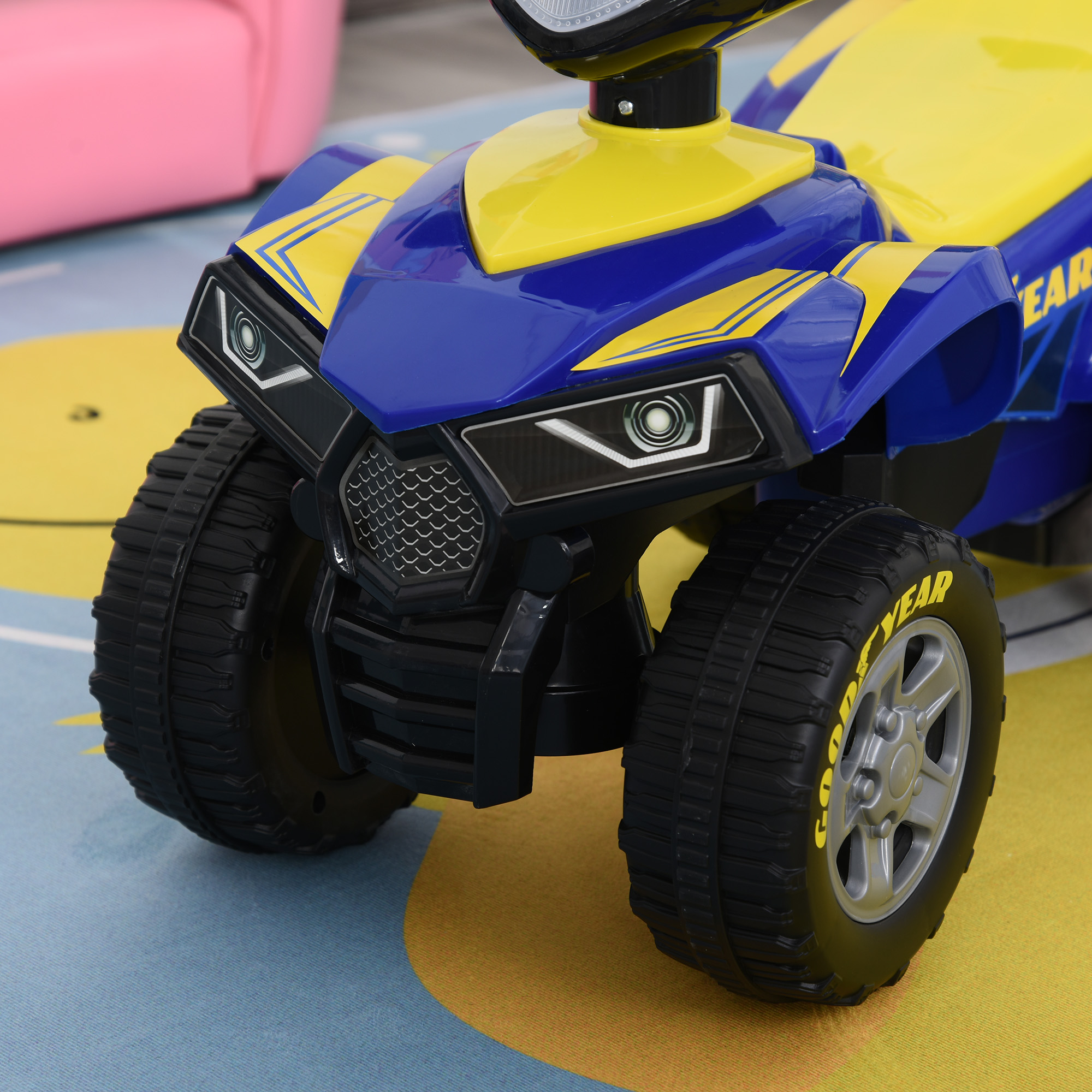 Un ATV giocattolo blu e giallo con 'GOODYEAR' sul pneumatico e una sedia rosa.