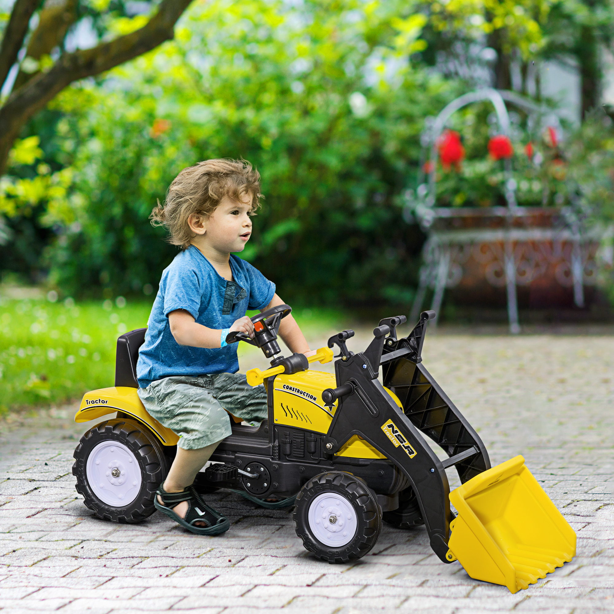 Un niño pequeño conduce un tractor de juguete amarillo en un camino de ladrillos. Detalles negros y cargador frontal.