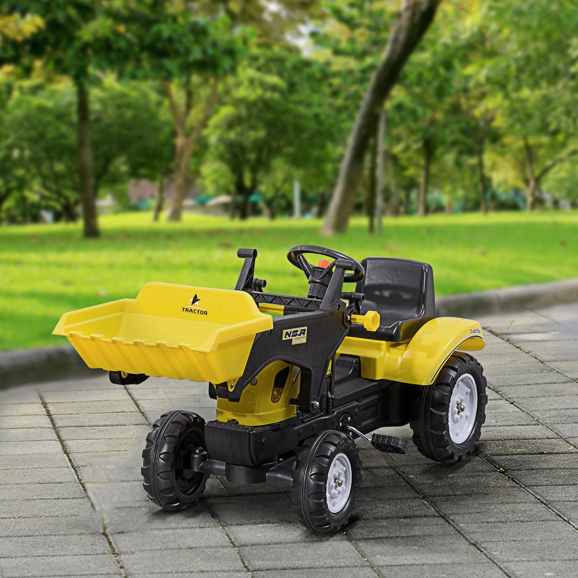 Trattore giocattolo giallo su superficie pavimentata, con erba verde e alberi sullo sfondo.