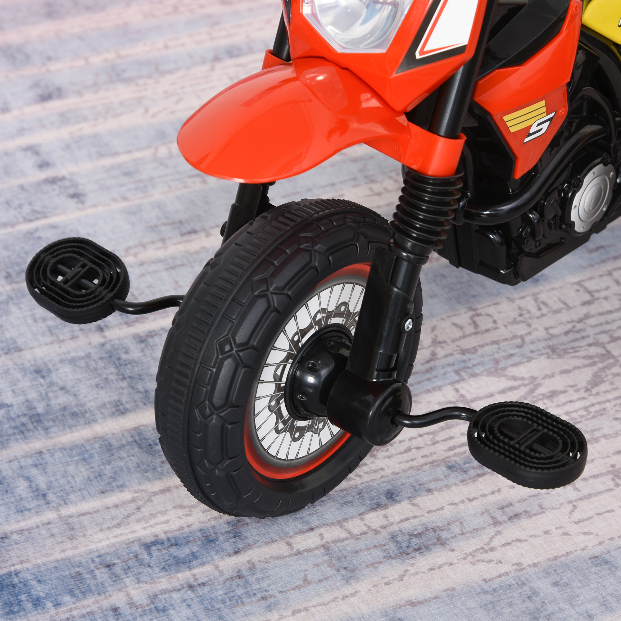 Primo piano della ruota di una moto giocattolo rossa e arancione, con pedali neri.
